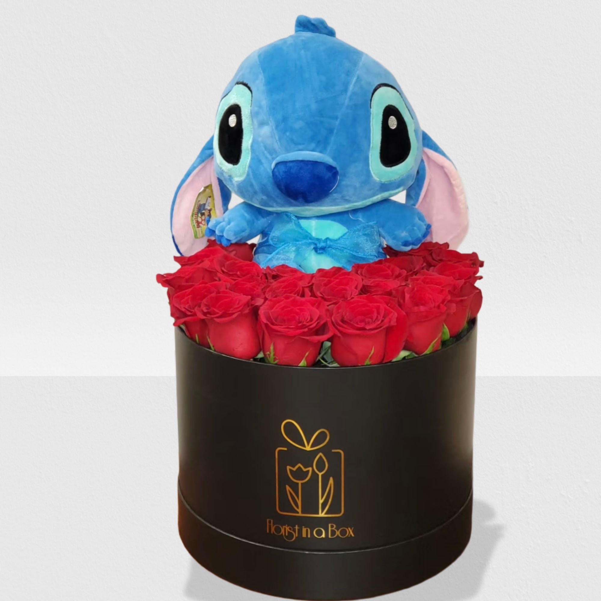 Round black hatbox filled with red roses topped with a large blue plush character toy.