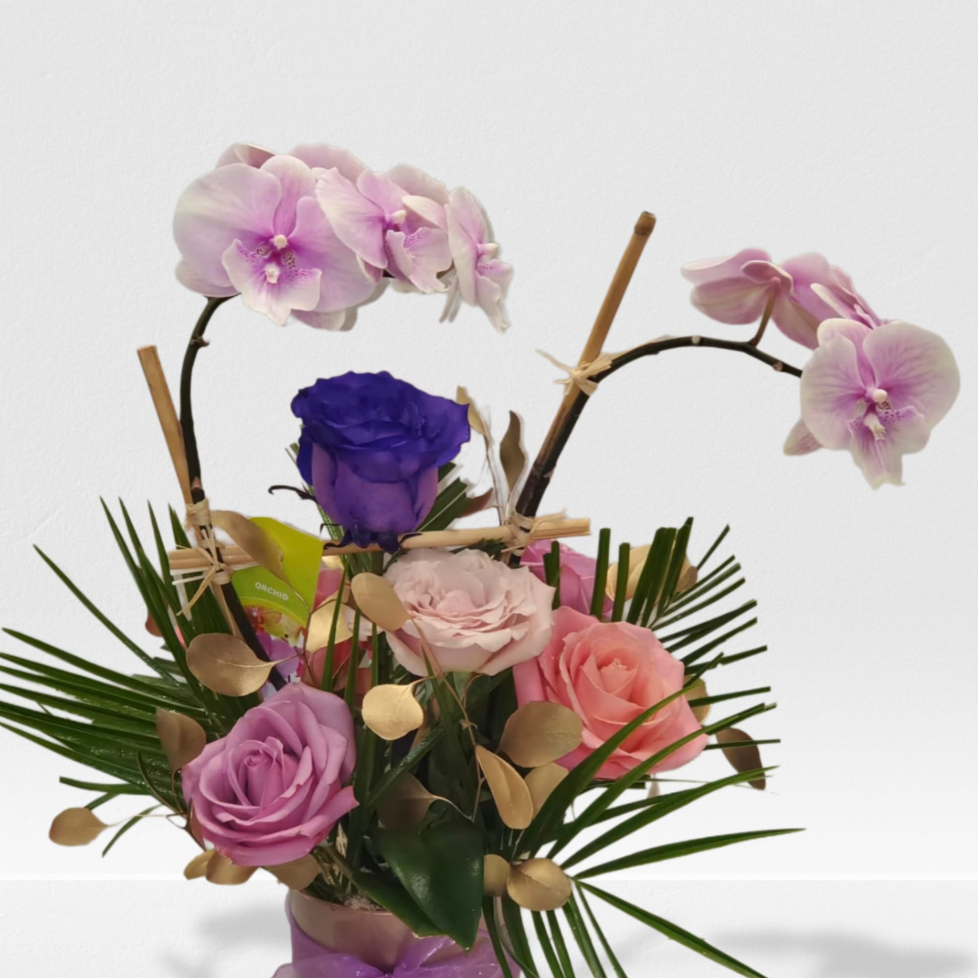 Arrangement of pink orchids and mixed roses in a cylinder vase with palm accents and a purple ribbon