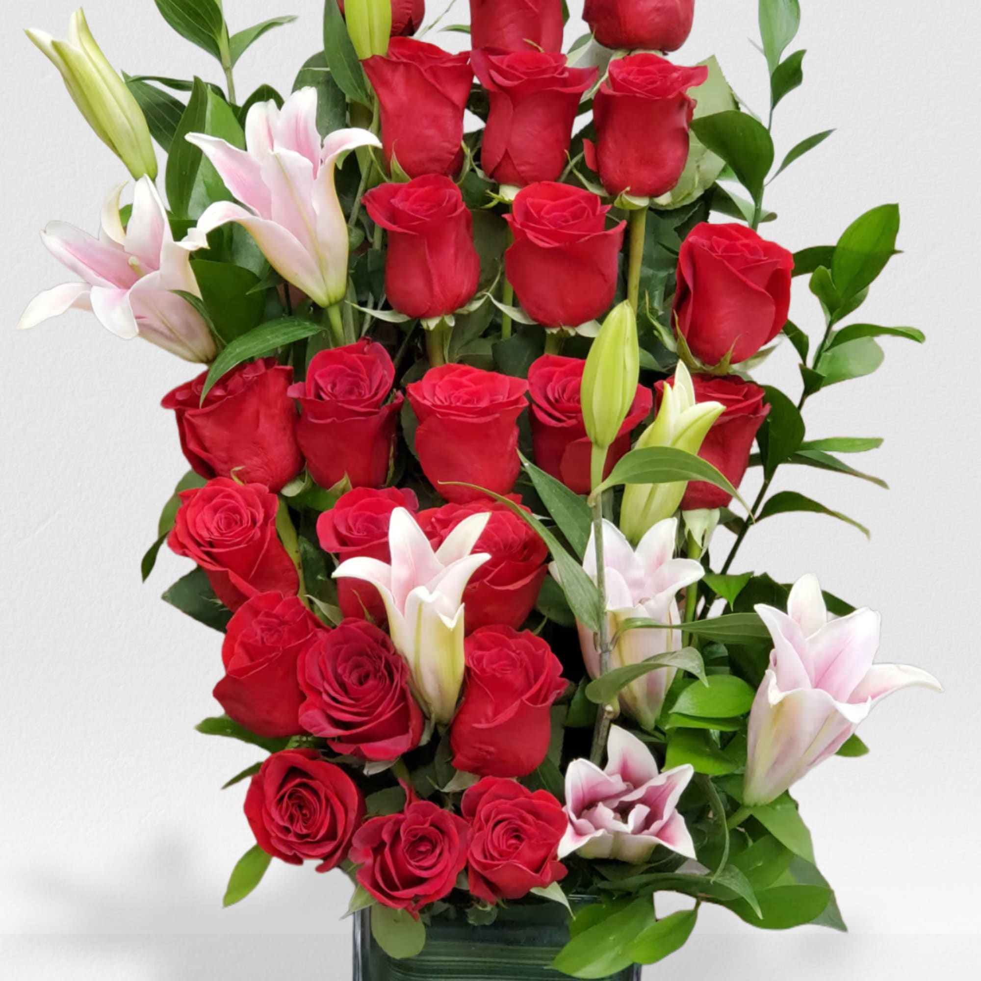 Tall arrangement of red roses and white lilies in a square glass vase