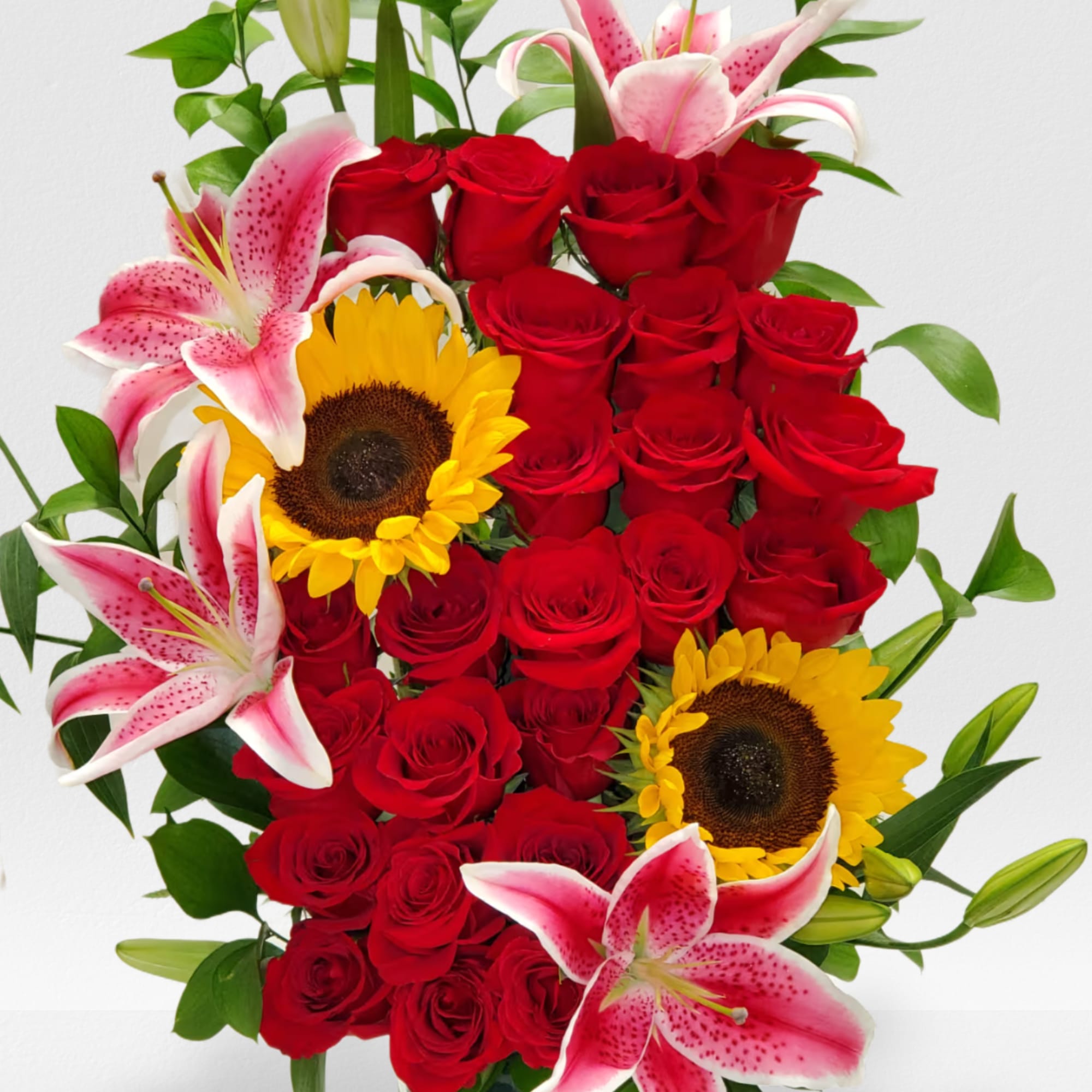 Tall arrangement of red roses with pink lilies and yellow sunflowers in a green glass vase