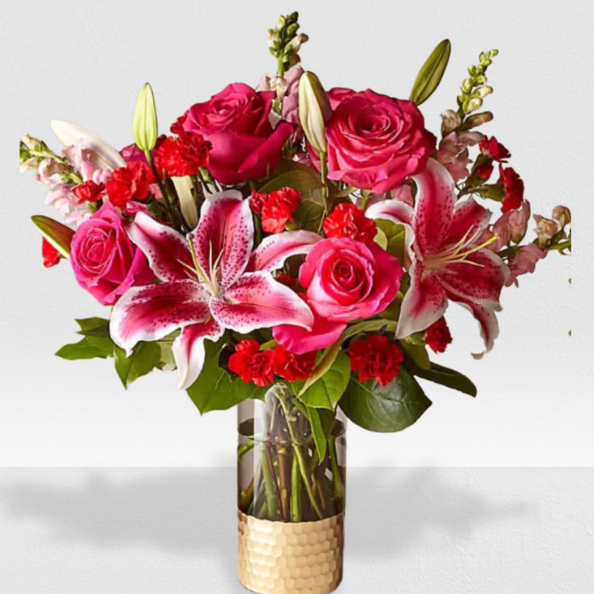 Pink lilies, hot pink roses, and red carnations in a clear vase with a gold base
