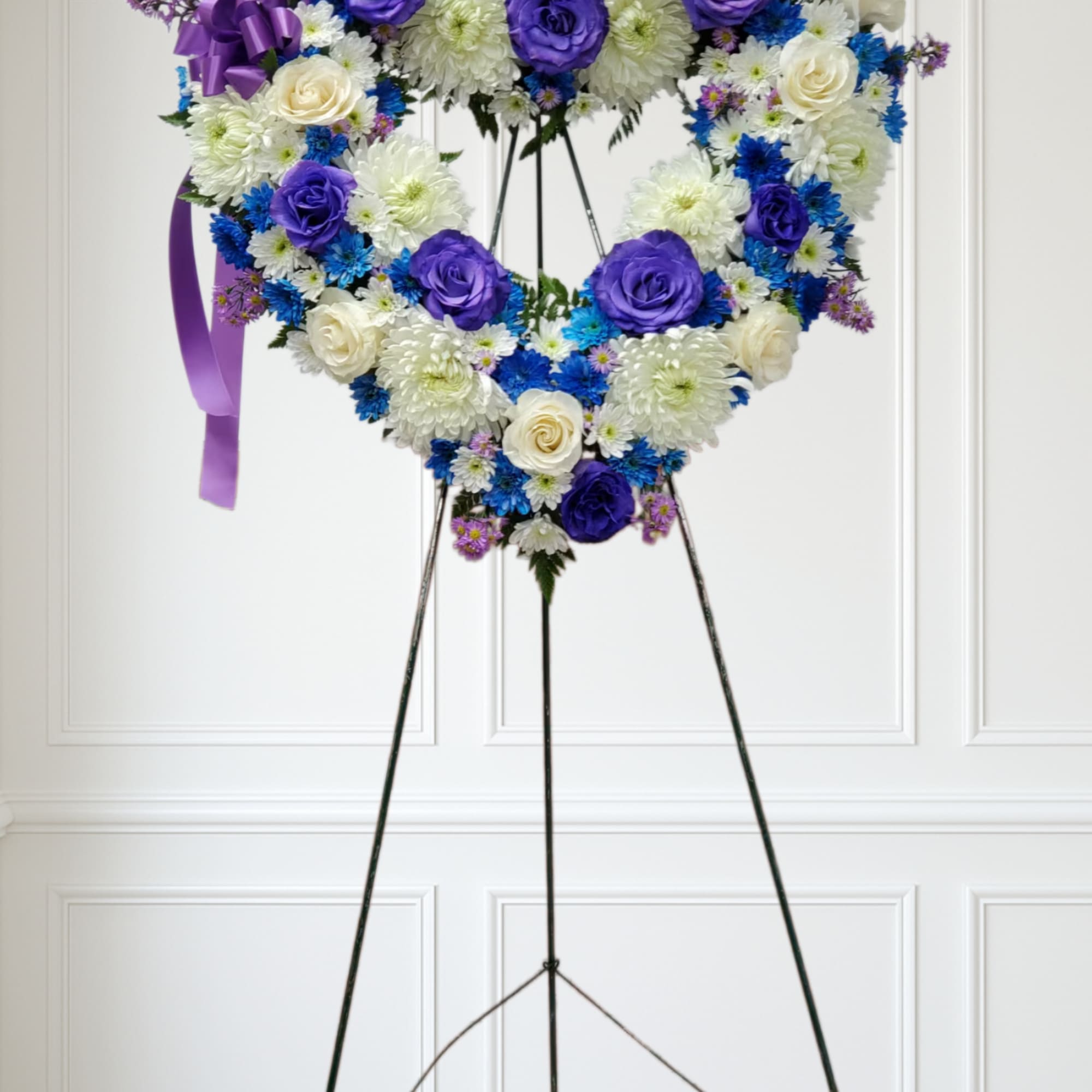 Heart-shaped standing wreath with purple, blue, and white flowers on a metal easel