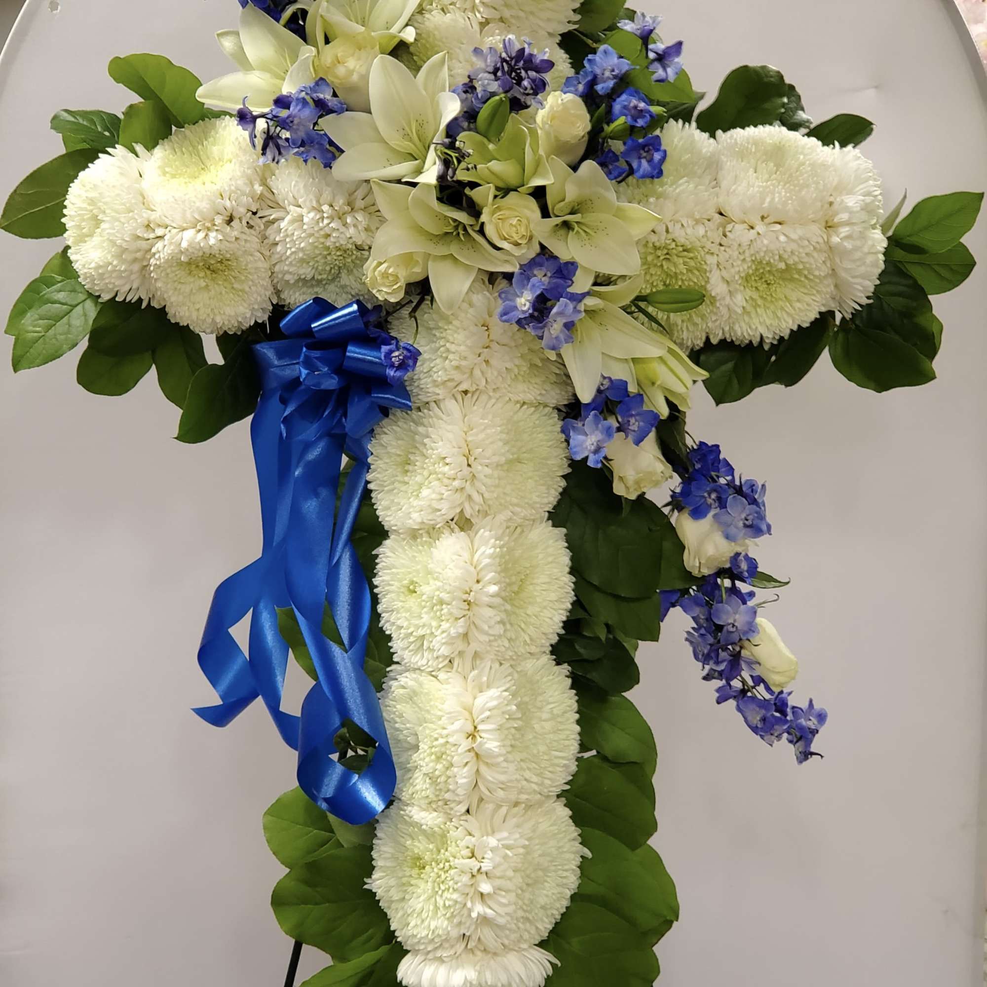 White floral cross arrangement with blue ribbon on an easel