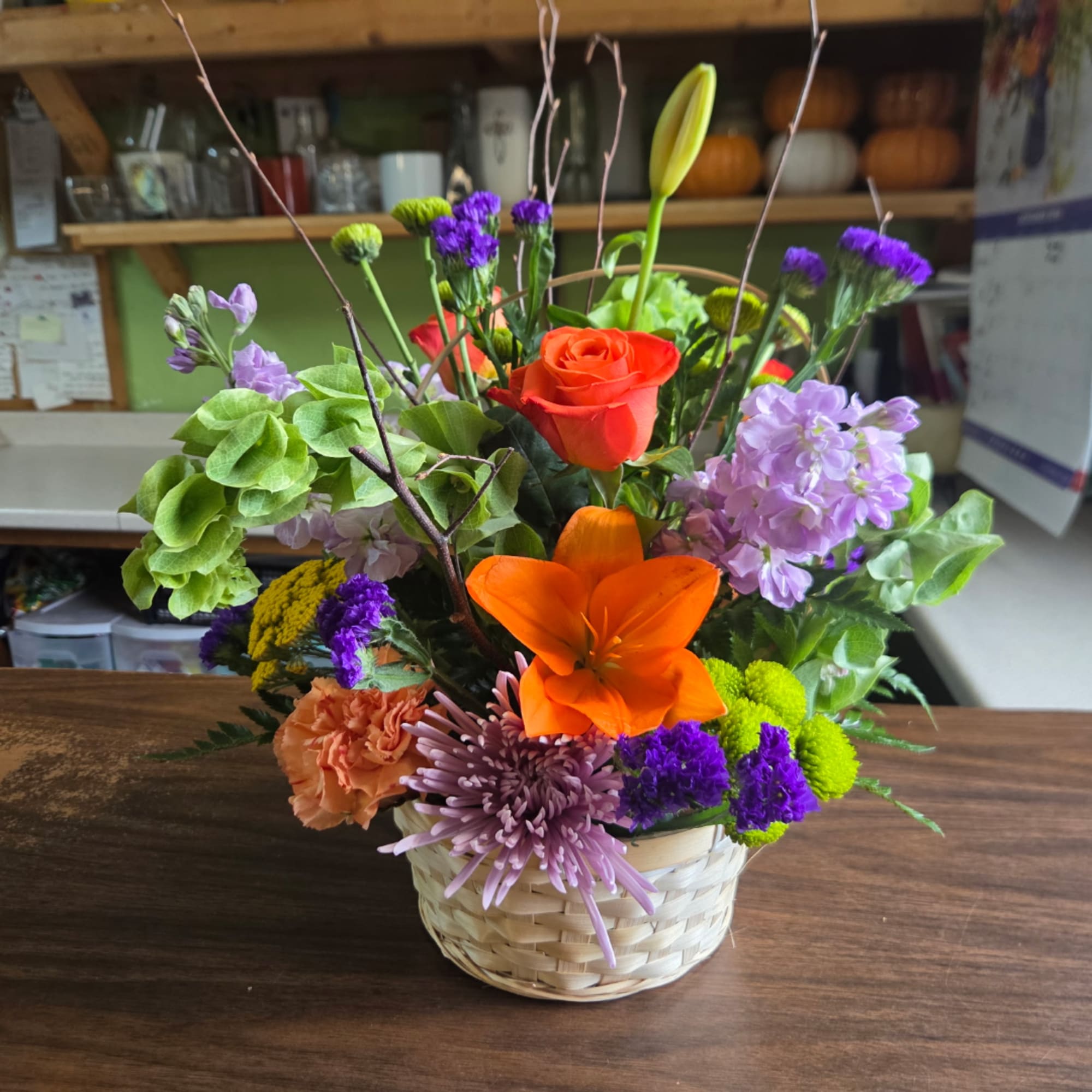 Mixed flower arrangement in a woven basket with orange and purple blooms, photo 2 of 3