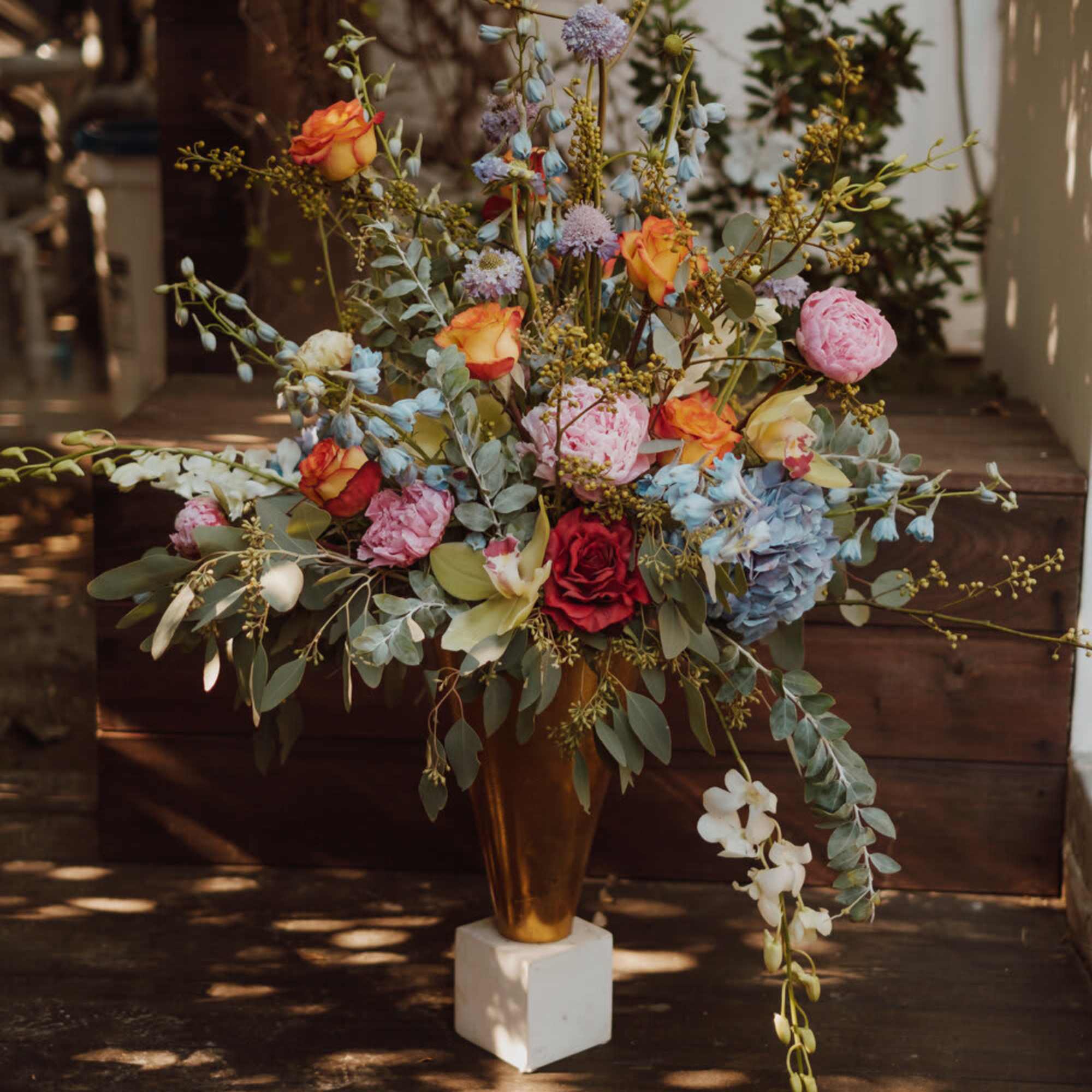Tall floral arrangement in a gold vase with pink, orange, blue, and white blooms