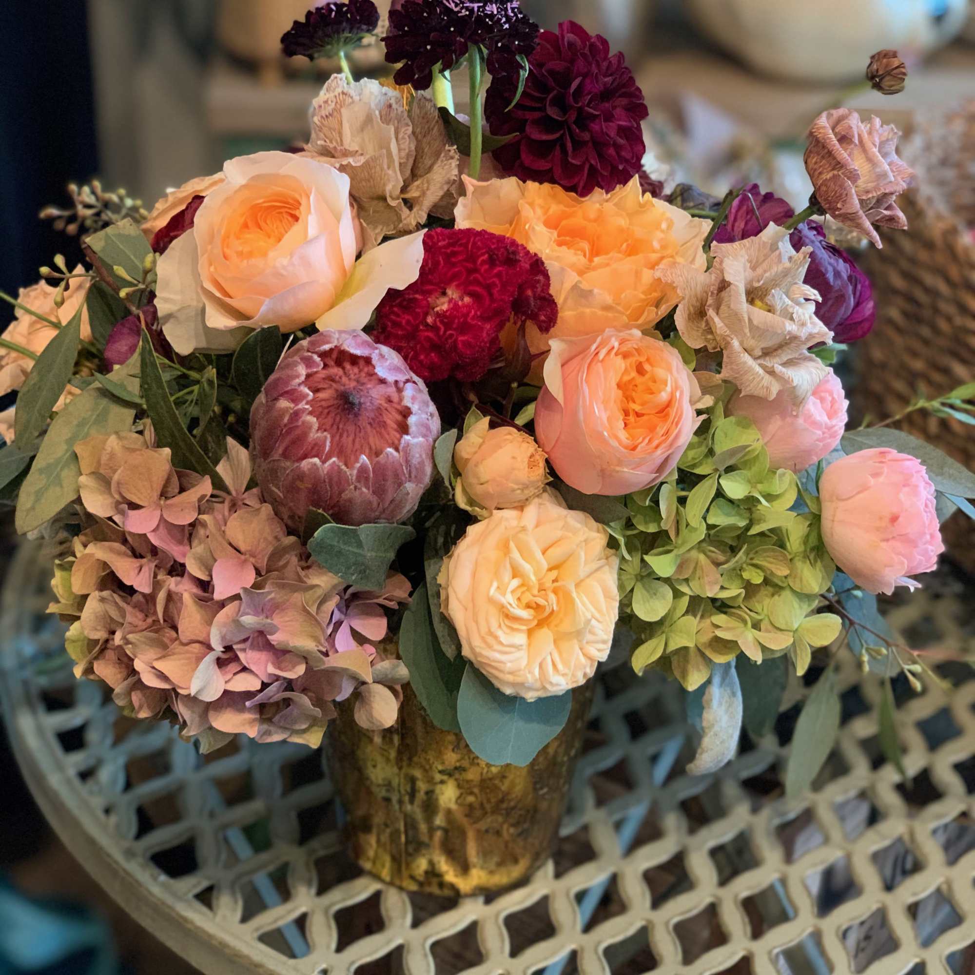 Bouquet of peach roses, burgundy blooms, and hydrangeas in a gold vase