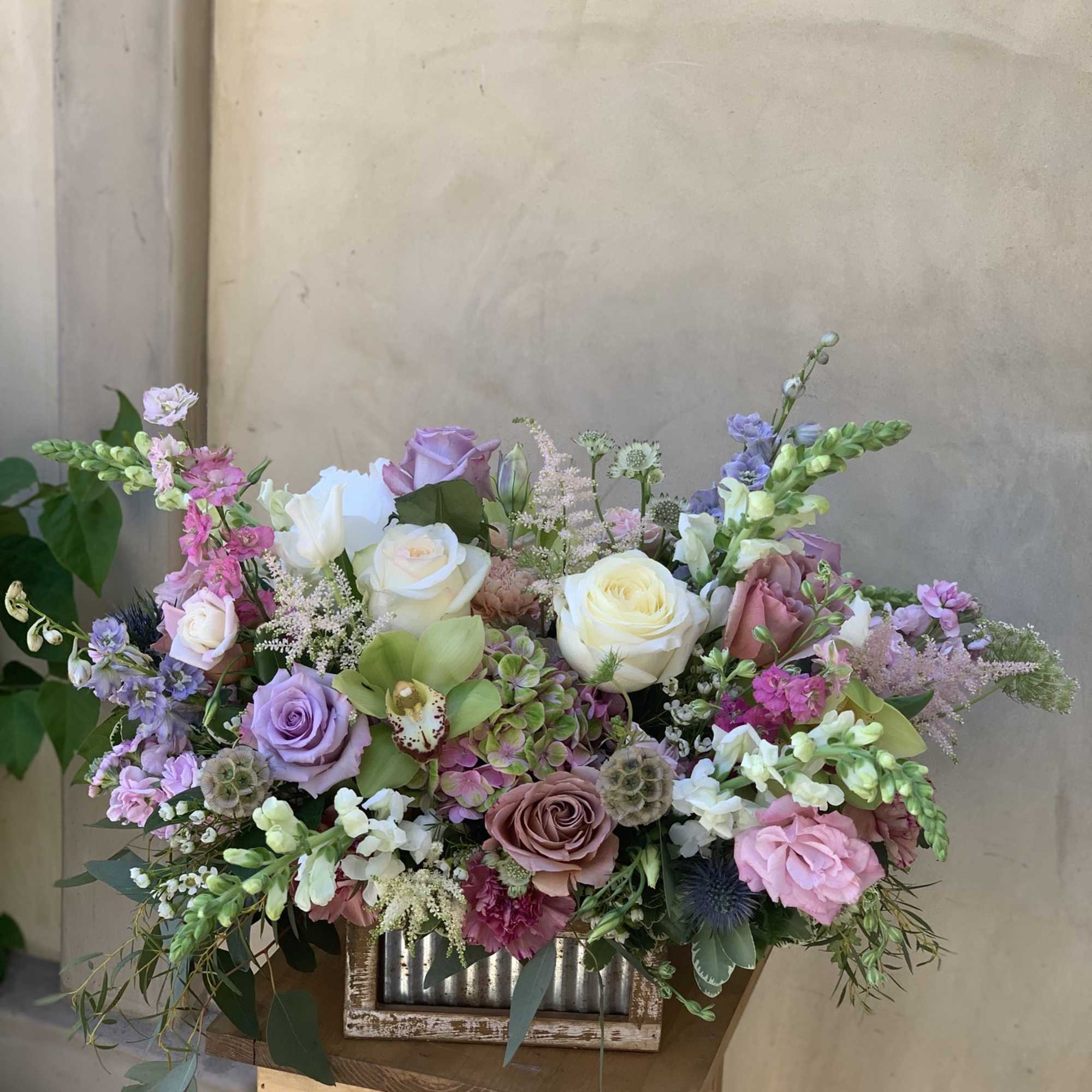 Large pastel floral arrangement with roses and mixed blooms in a rustic container