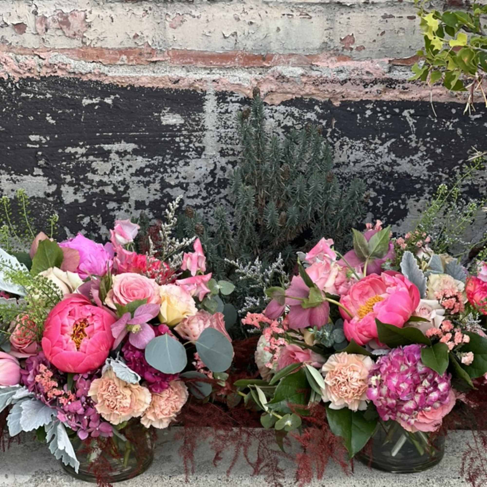 Two pink floral arrangements in glass vases with peonies and roses