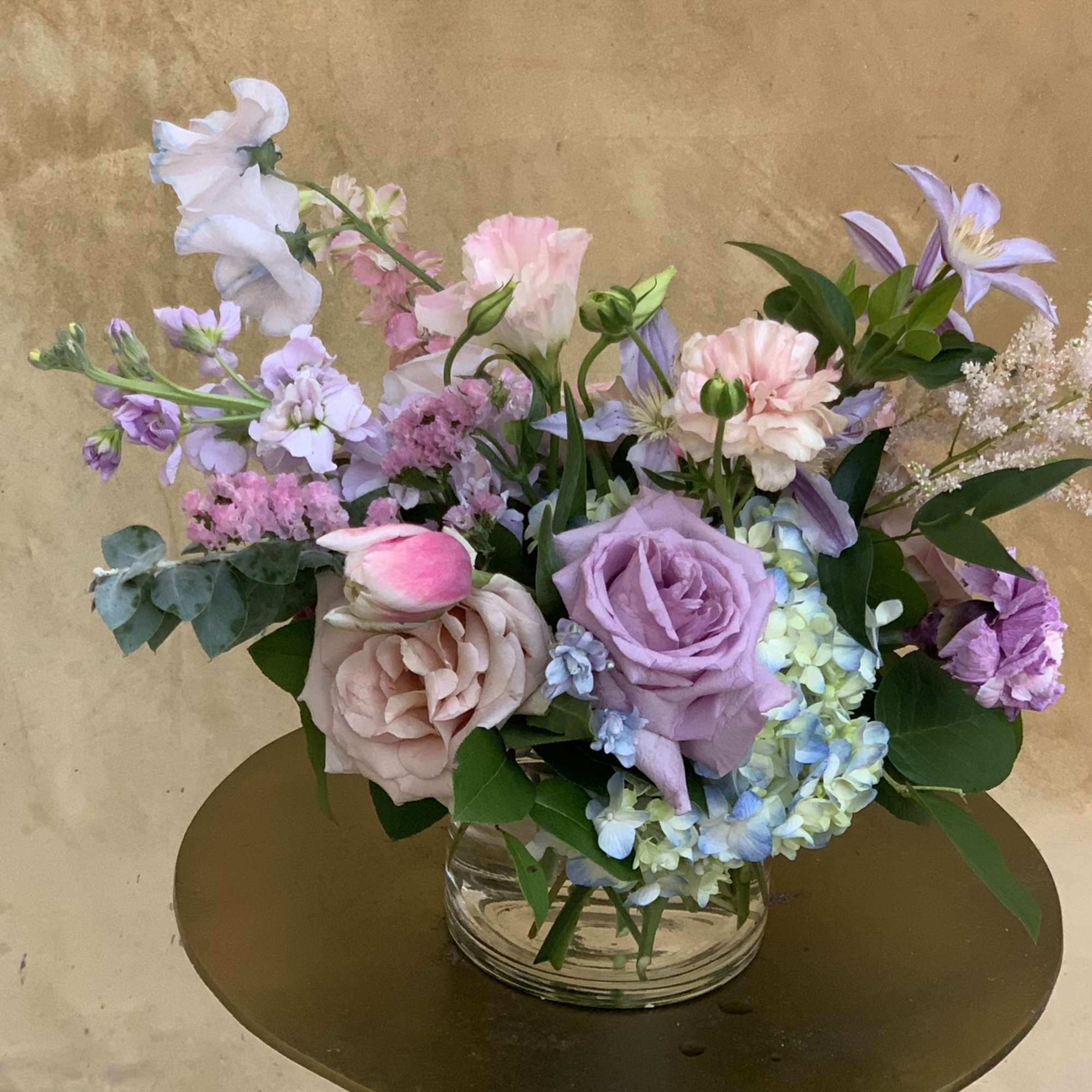 Pastel bouquet of roses, hydrangea, and lilac flowers in a clear glass vase