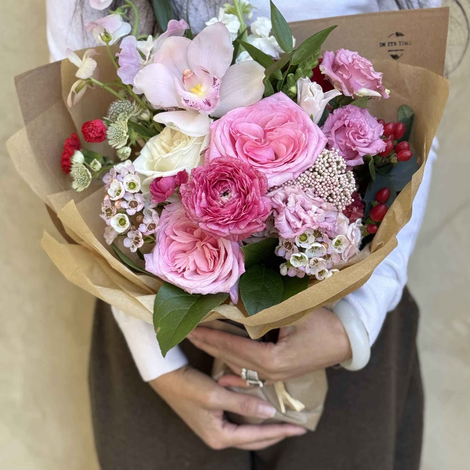 Handheld bouquet of pink and white flowers wrapped in brown paper