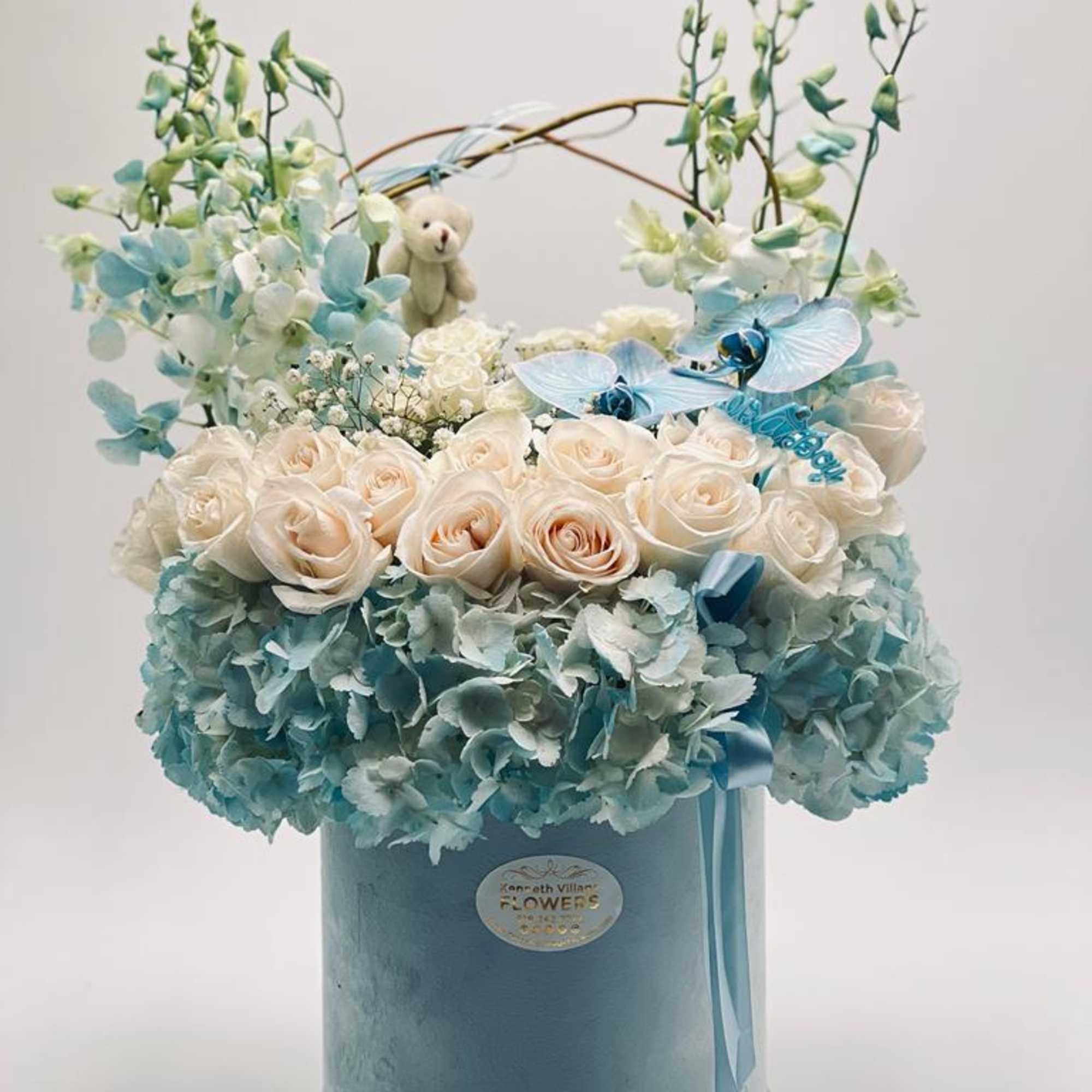 Blue hatbox arrangement with cream roses and pale blue flowers