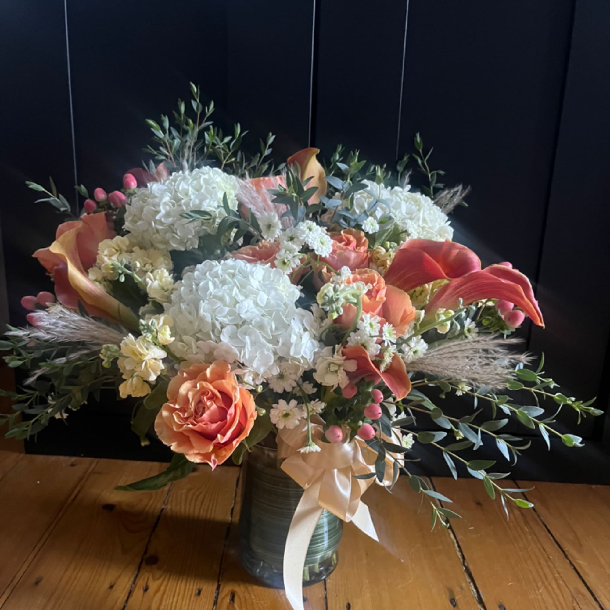 Peach and white floral arrangement in a glass vase with a ribbon