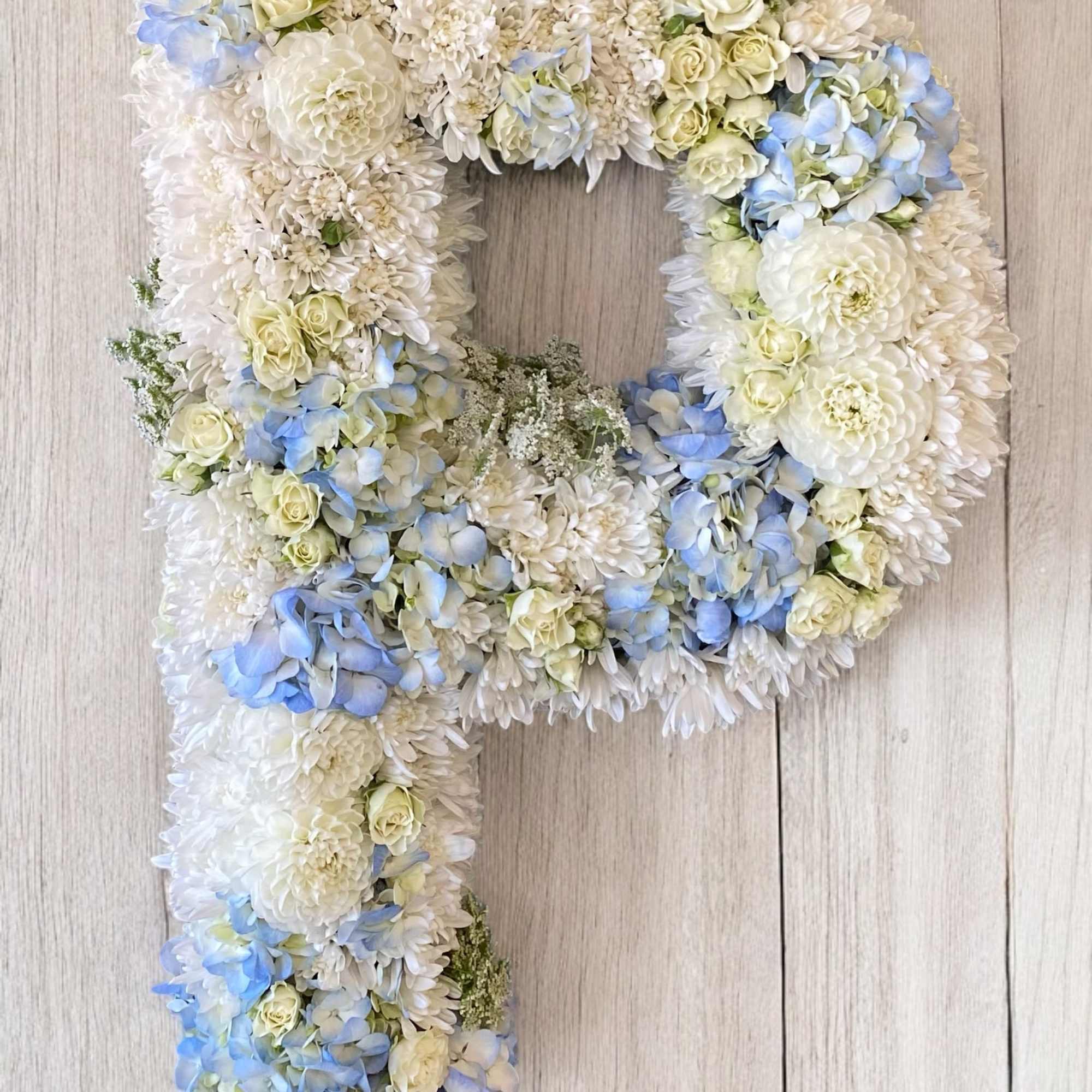Floral arrangement shaped like a letter P in white, cream, and pale blue