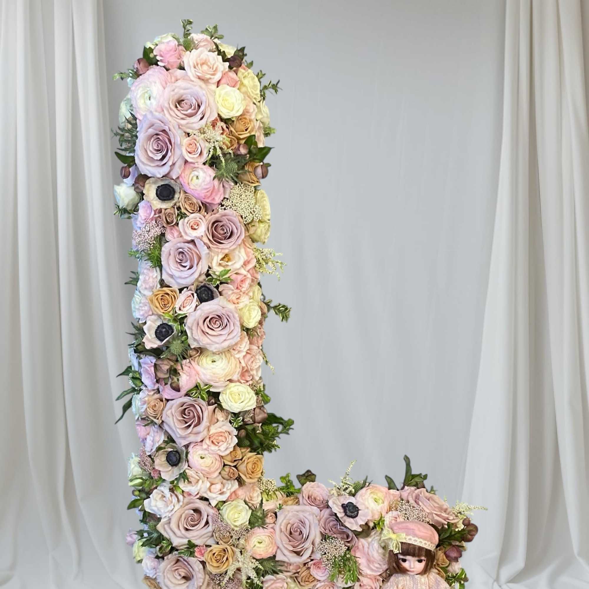 Tall floral letter L with pastel roses and a doll at the base