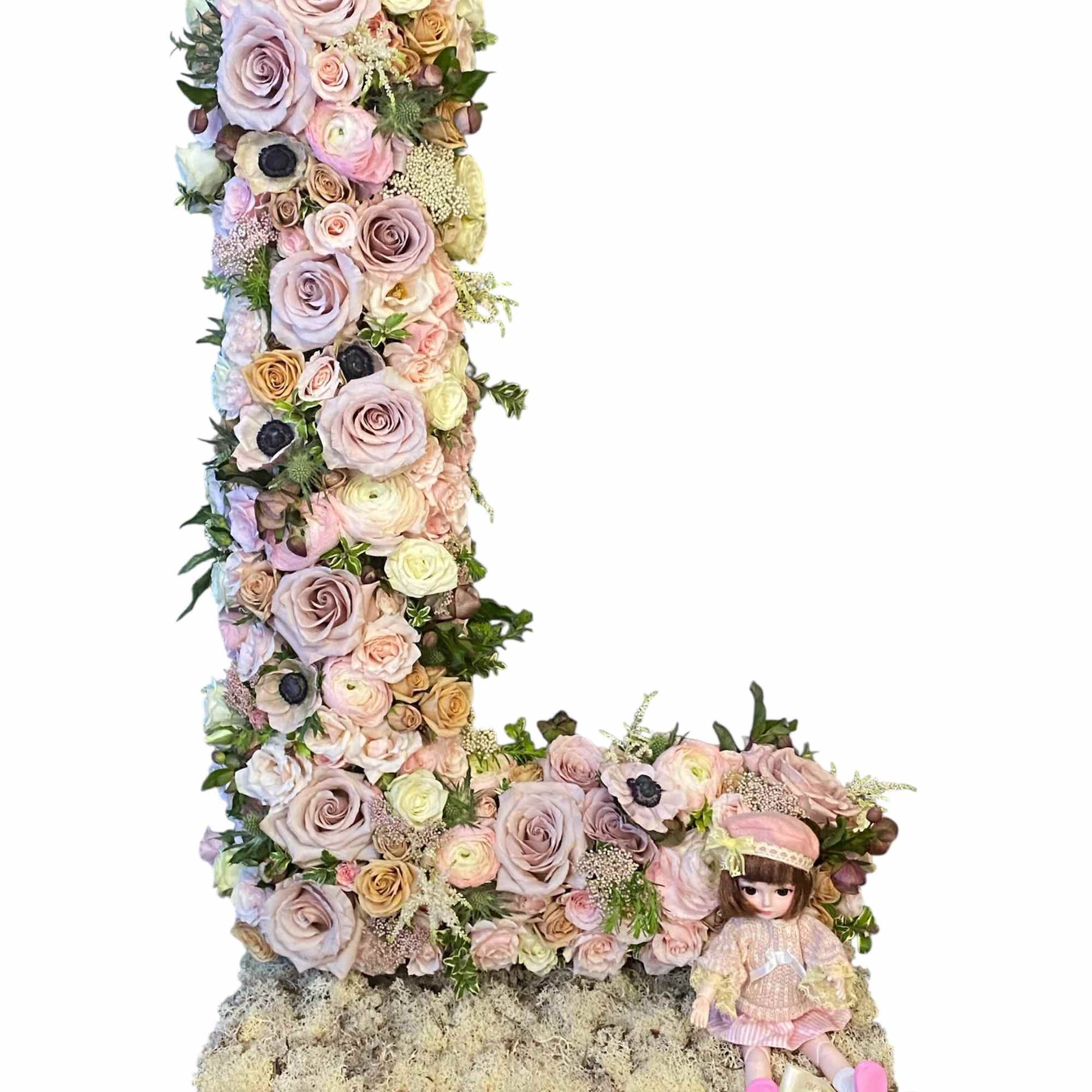 Floral letter L made of pastel roses with a small doll sitting beside it