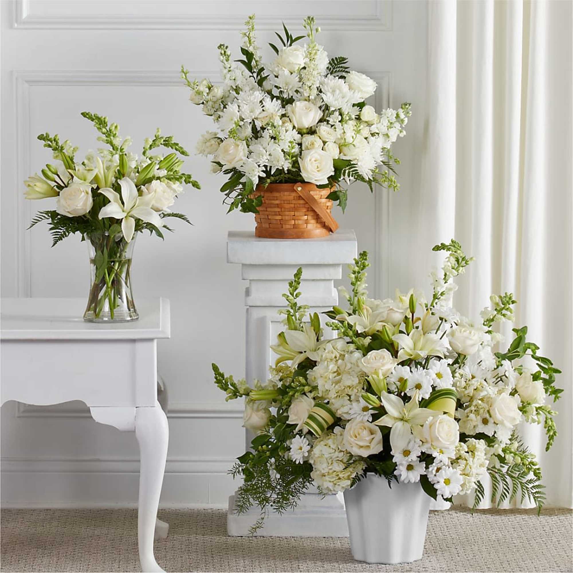 Three white floral arrangements in vases and a basket