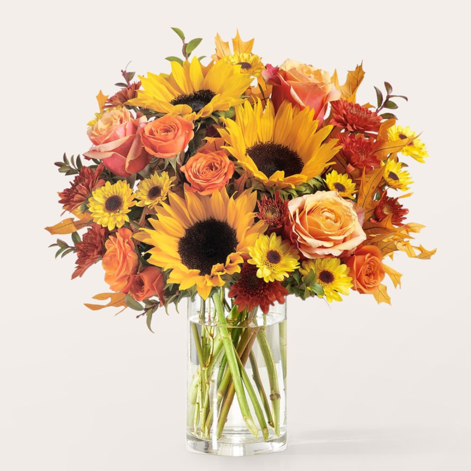 Bouquet of sunflowers, roses, and mums in a clear glass vase