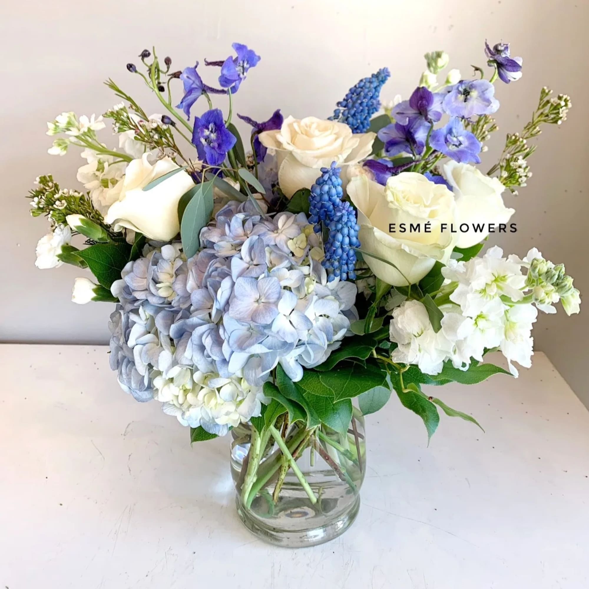 Bouquet of white roses, blue hydrangeas, and purple flowers in a glass vase