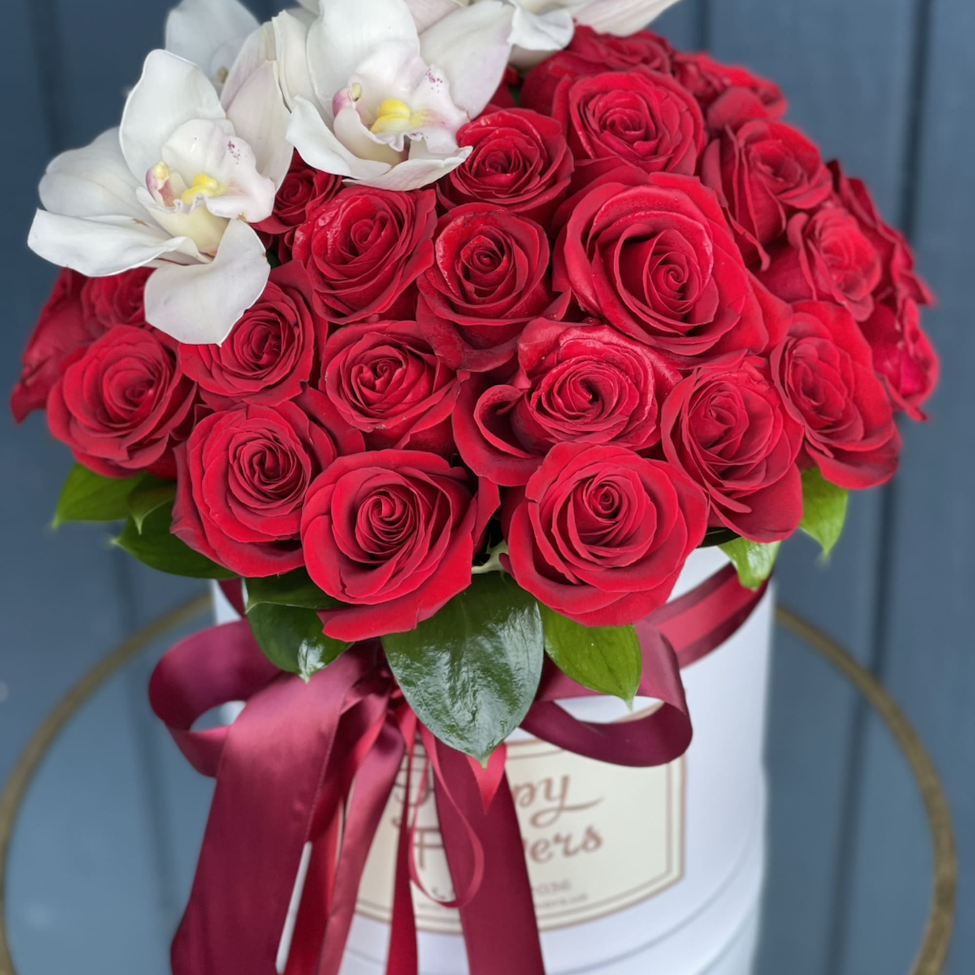 Red roses with white orchids in a white hatbox tied with a ribbon
