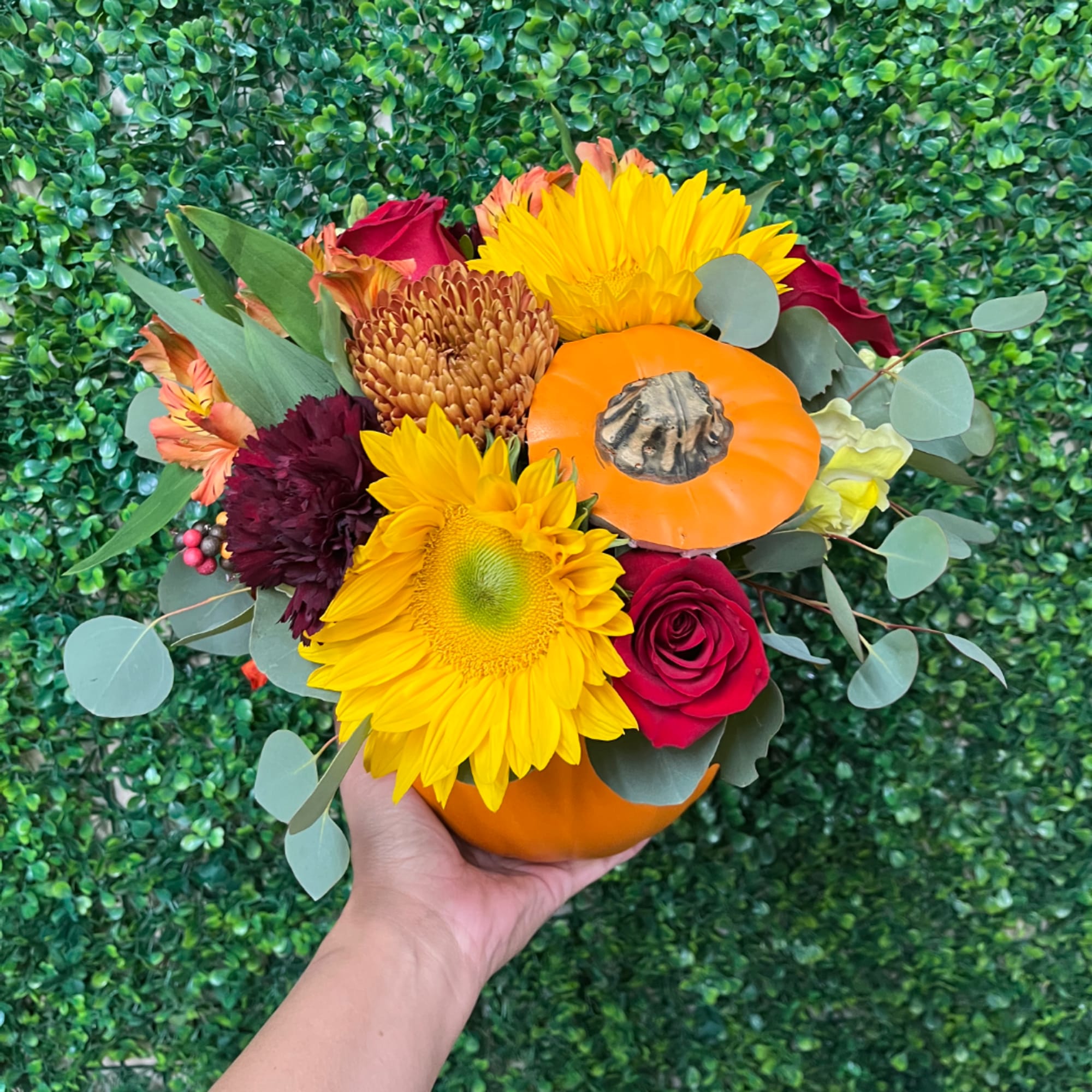 Handheld bouquet with sunflowers, red roses, and an orange pumpkin accent