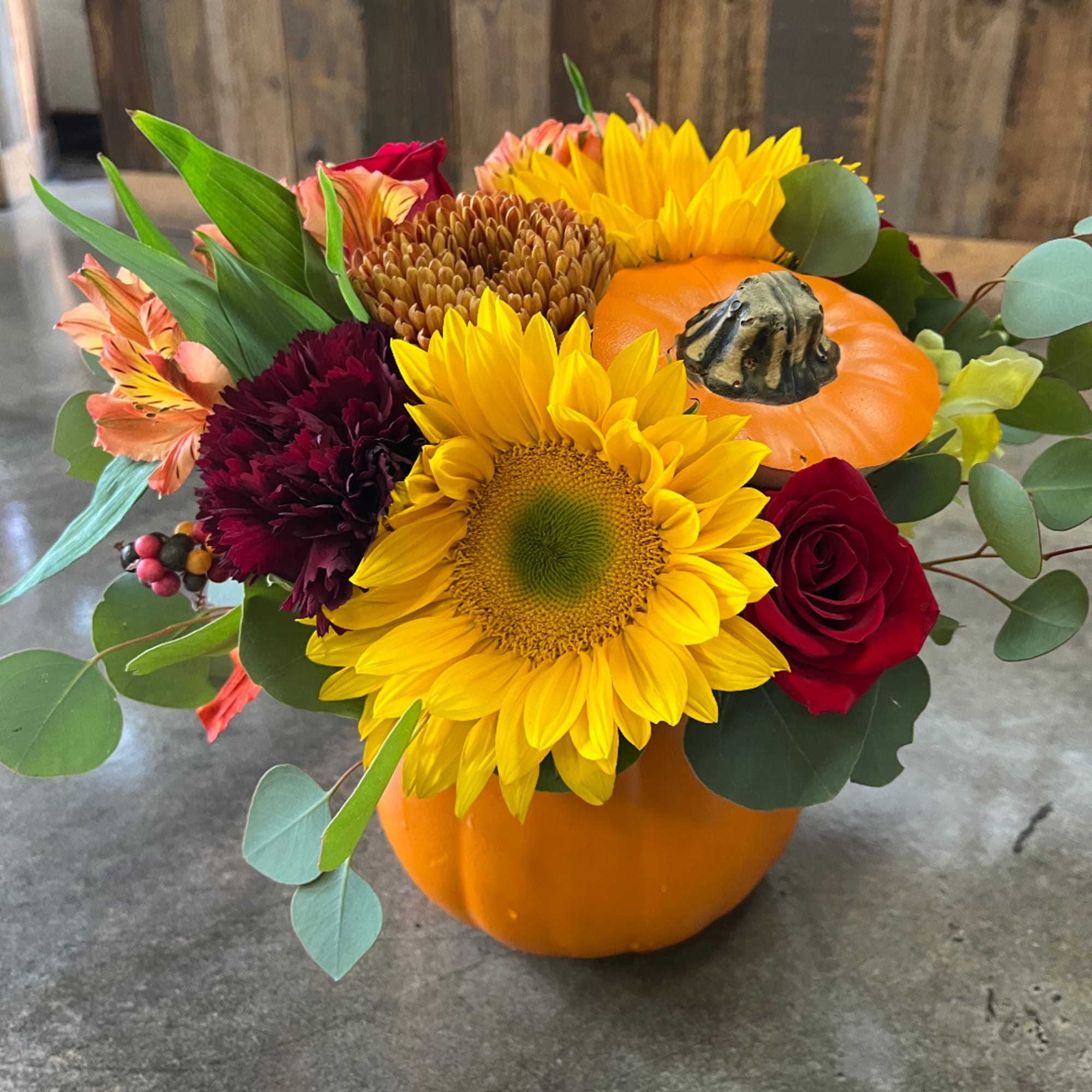 Fall bouquet in a pumpkin vase with sunflowers, roses, and mums