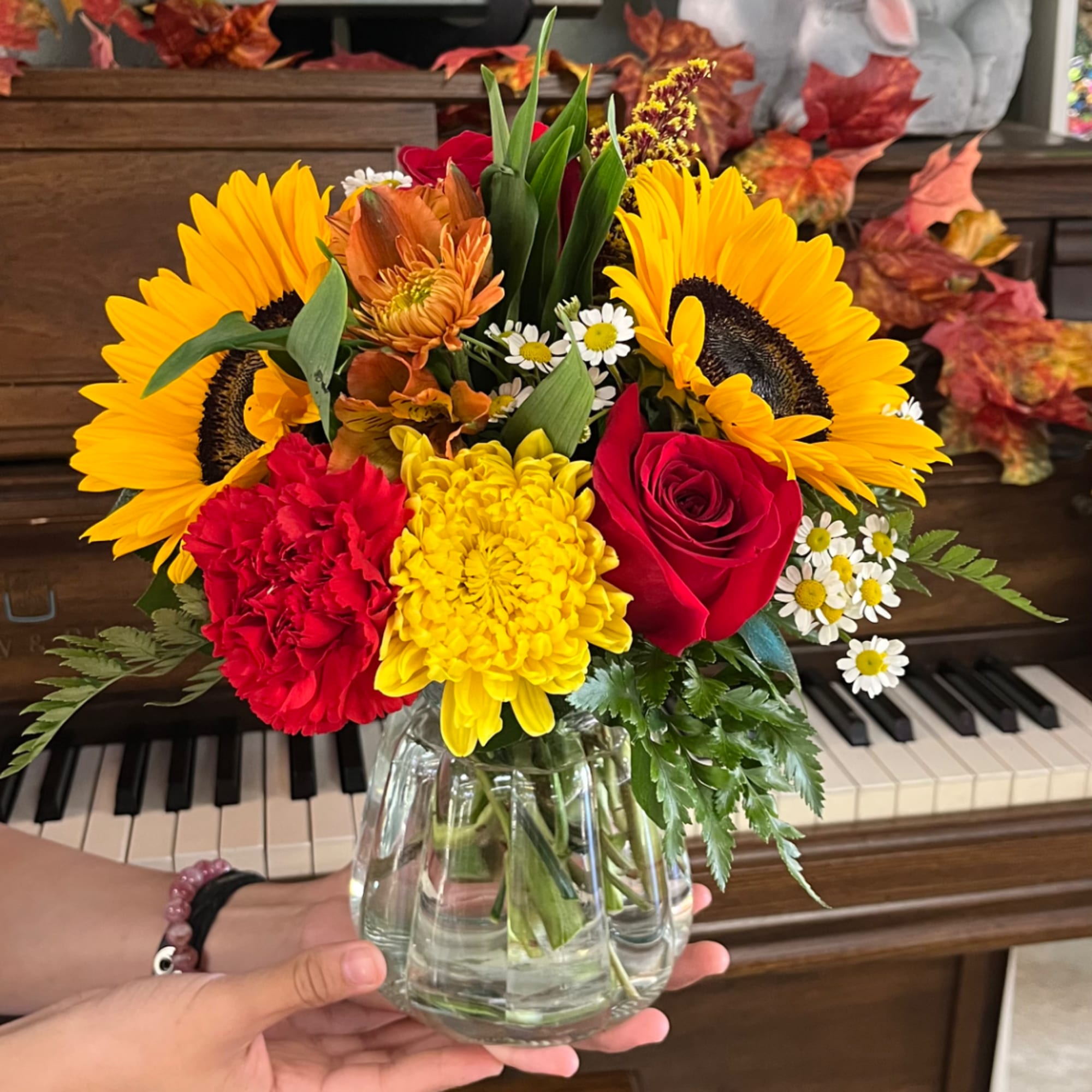 Bright mixed bouquet in a clear glass vase with sunflowers, roses, and mums