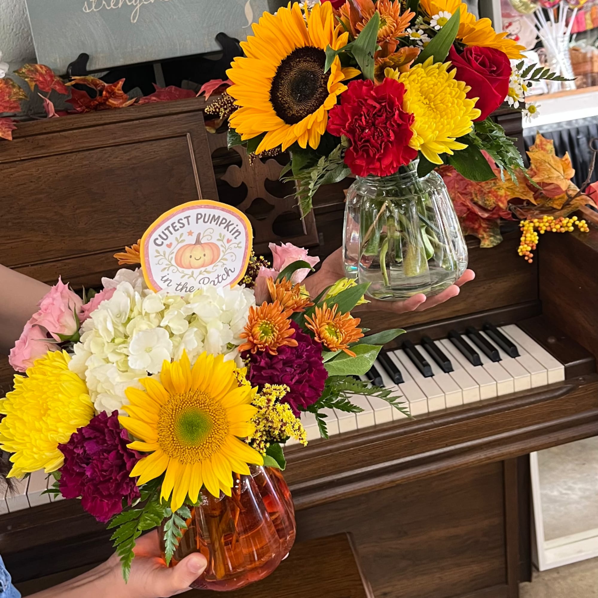 Two fall flower arrangements with sunflowers, mums, and hydrangea in glass vases