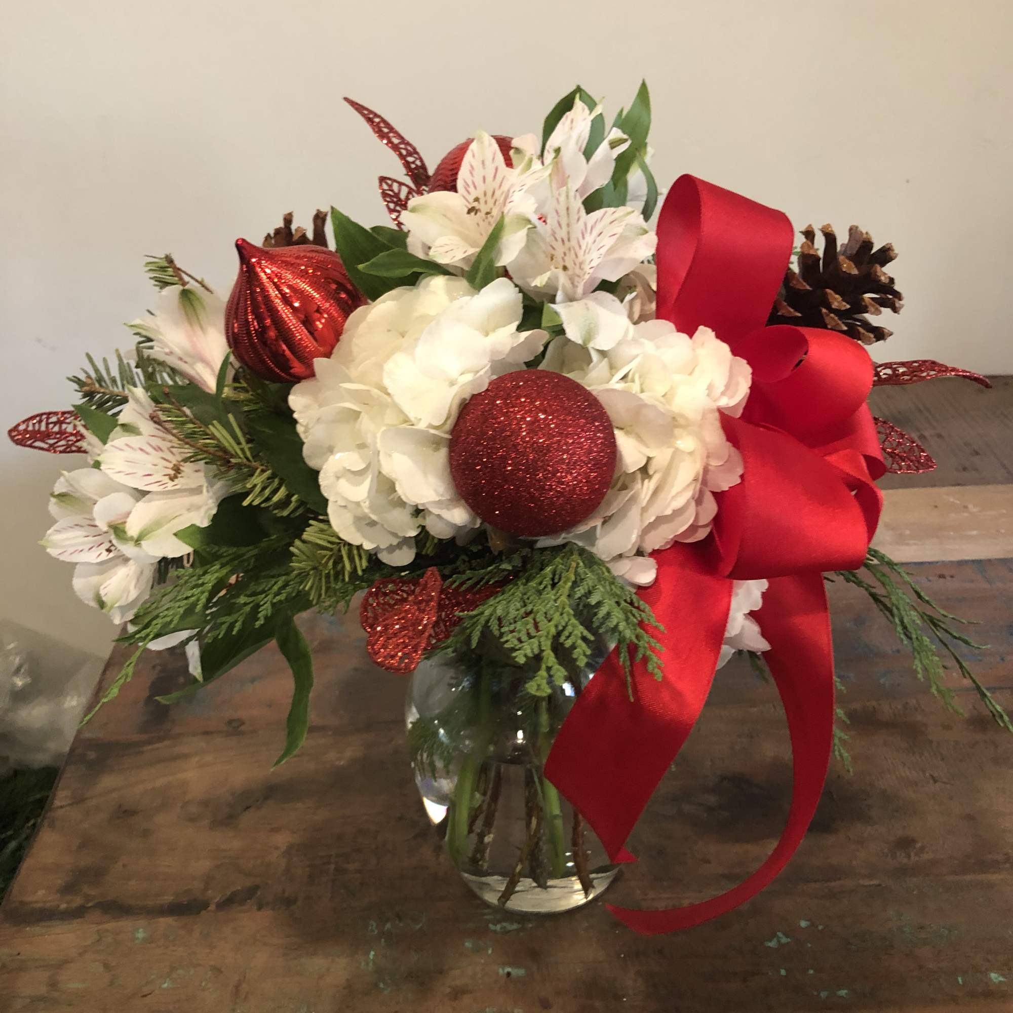Holiday bouquet of white flowers with red ornaments and a large red ribbon in a glass vase