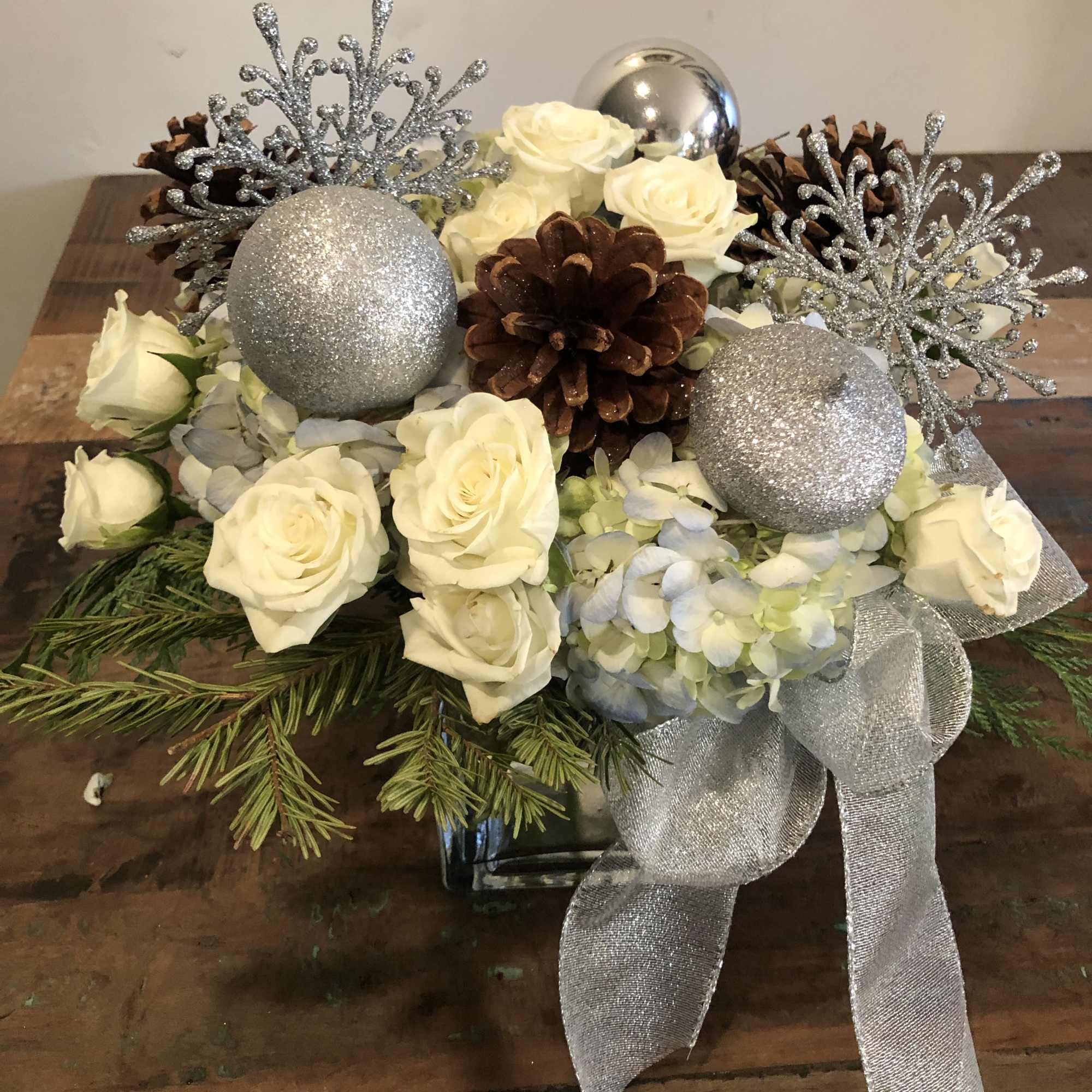 White roses and hydrangeas with silver ornaments and pinecones in a low arrangement