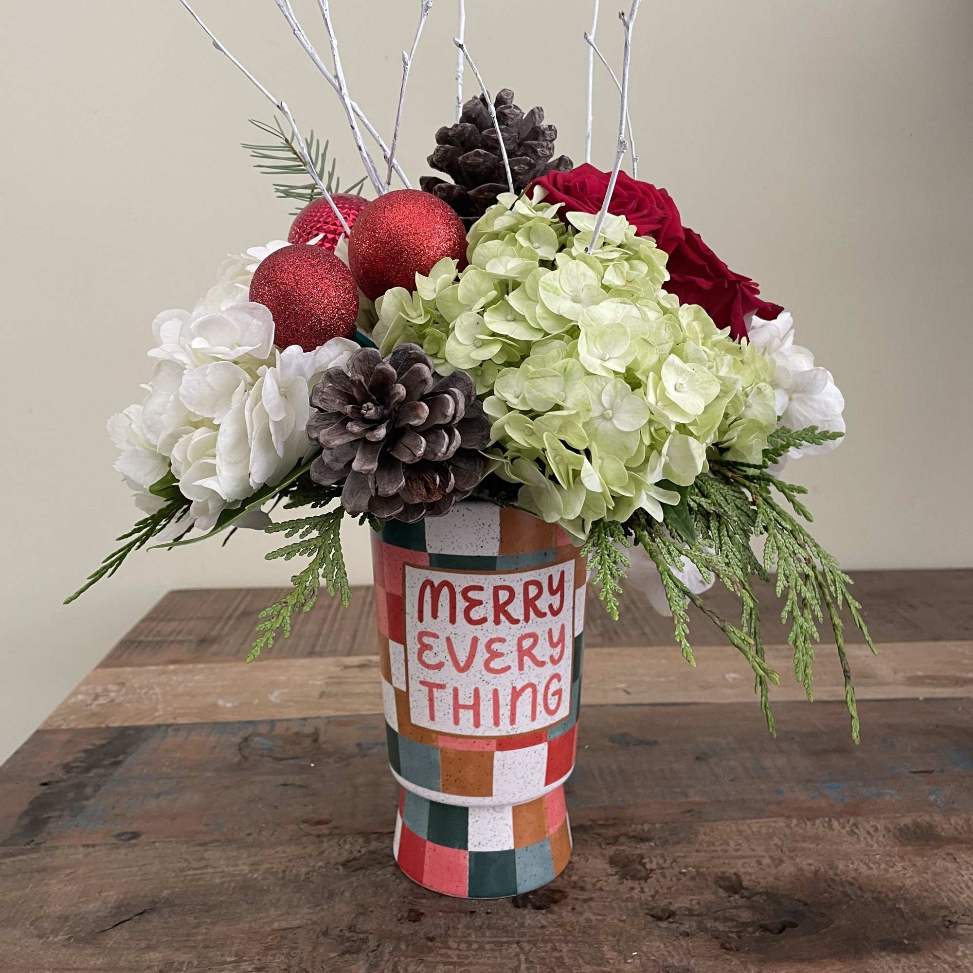 Holiday floral arrangement in a patterned vase with red ornaments and pinecones