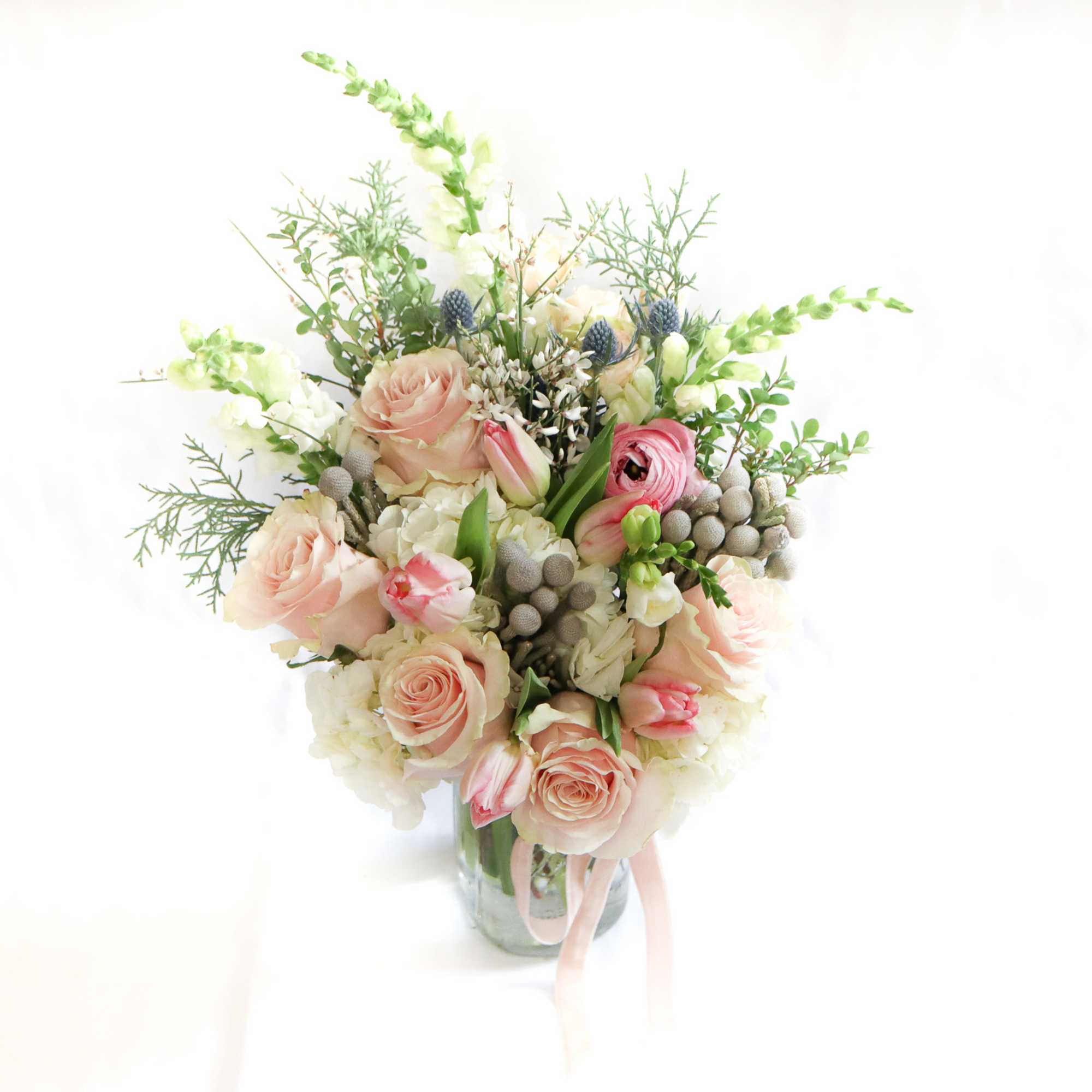 Blush roses and pink ranunculus in a glass vase with airy greenery