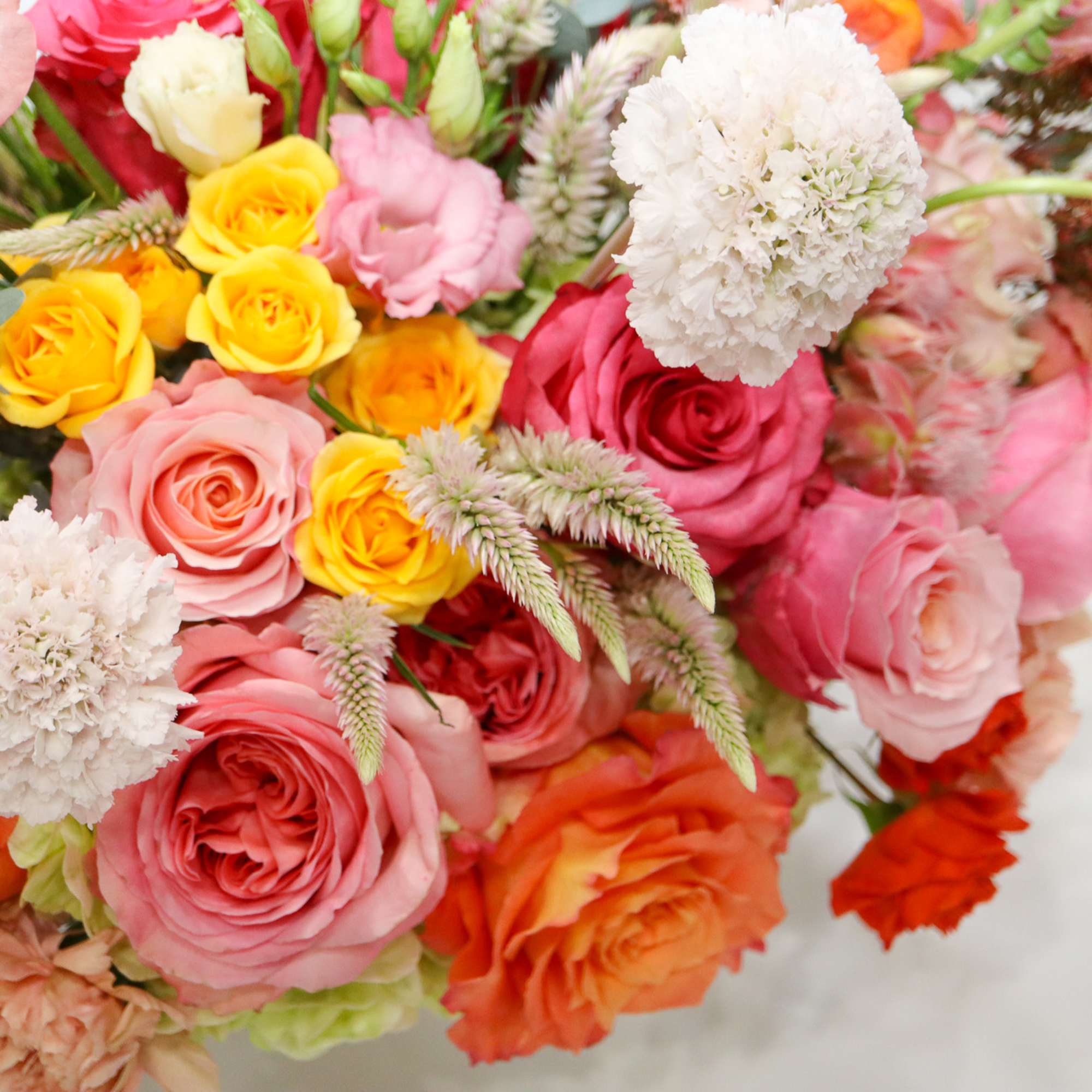 Mixed bouquet of roses and white pom-pom flowers in pink, yellow, and orange