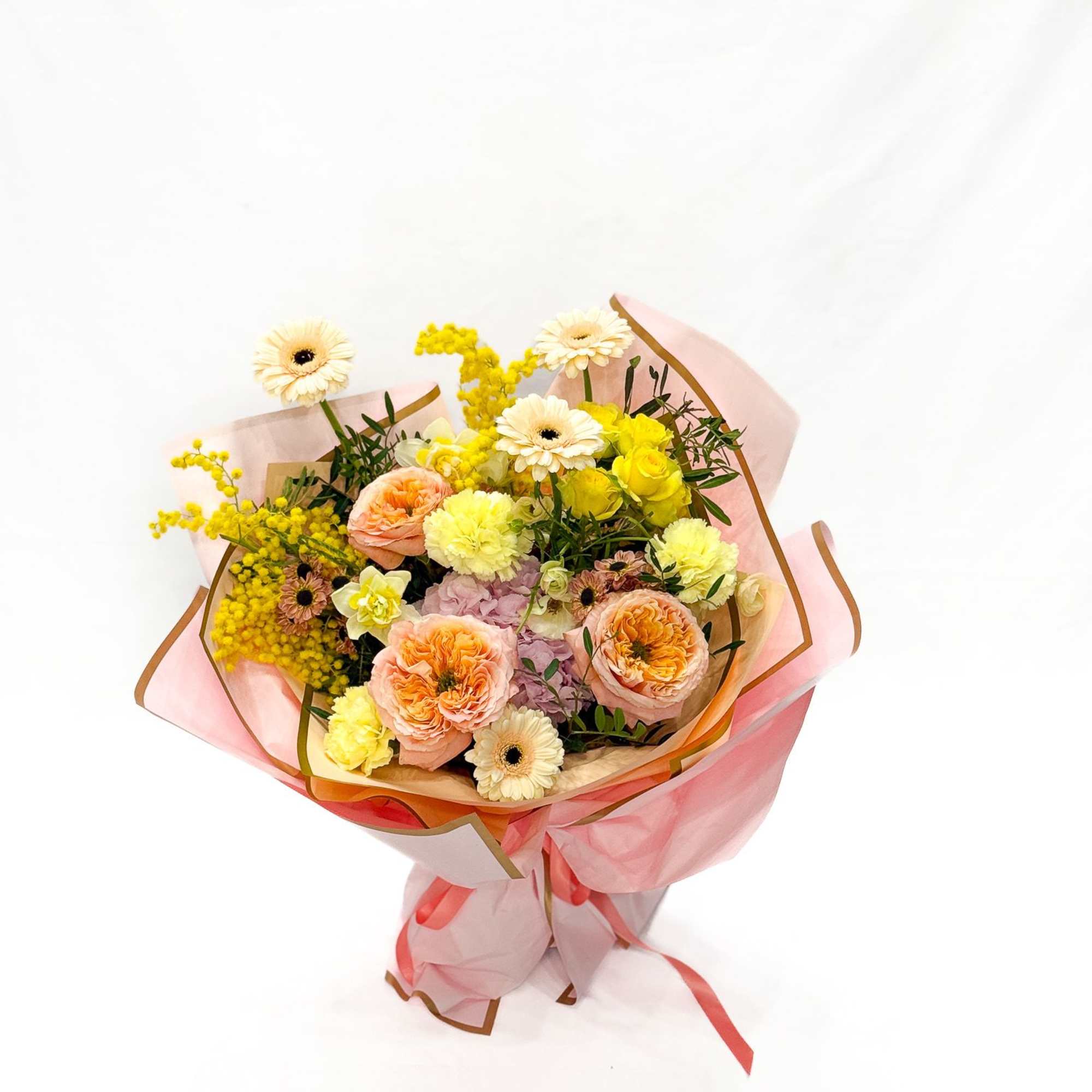 Bouquet of peach, yellow, and white flowers wrapped in pink paper
