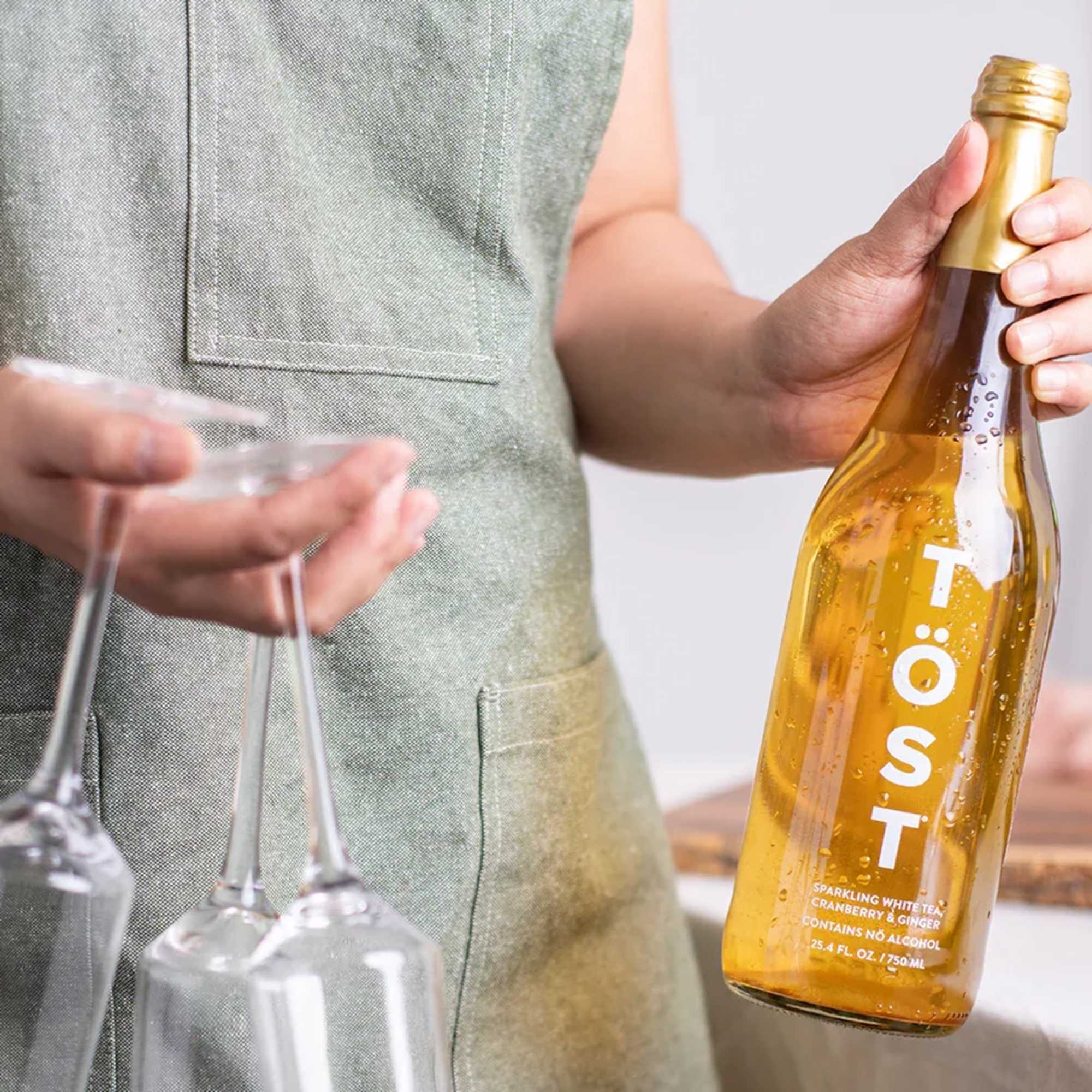 Person holding a bottle of sparkling tea beside two stemmed glasses