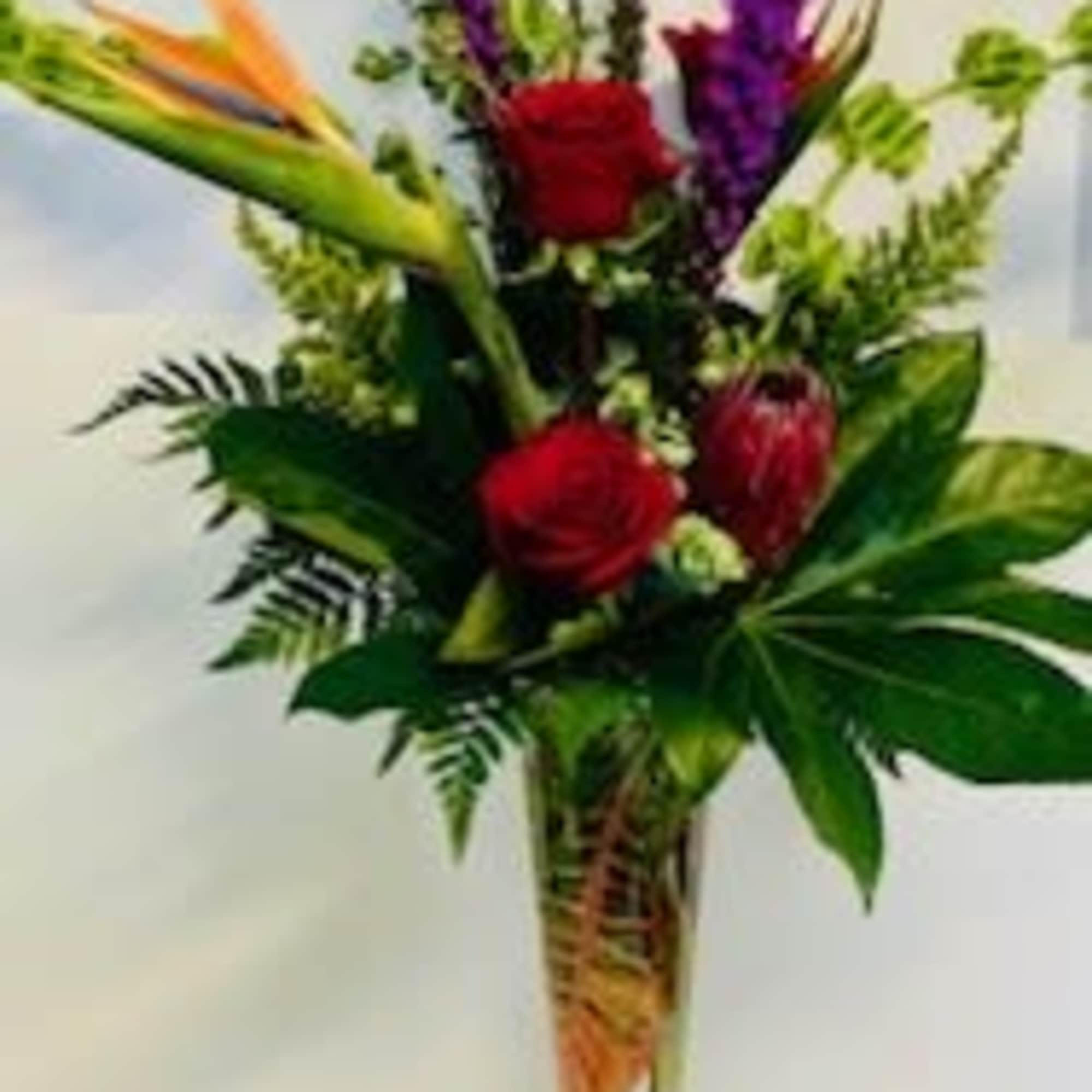 Tropical bouquet with red roses and purple spikes in a tall glass vase