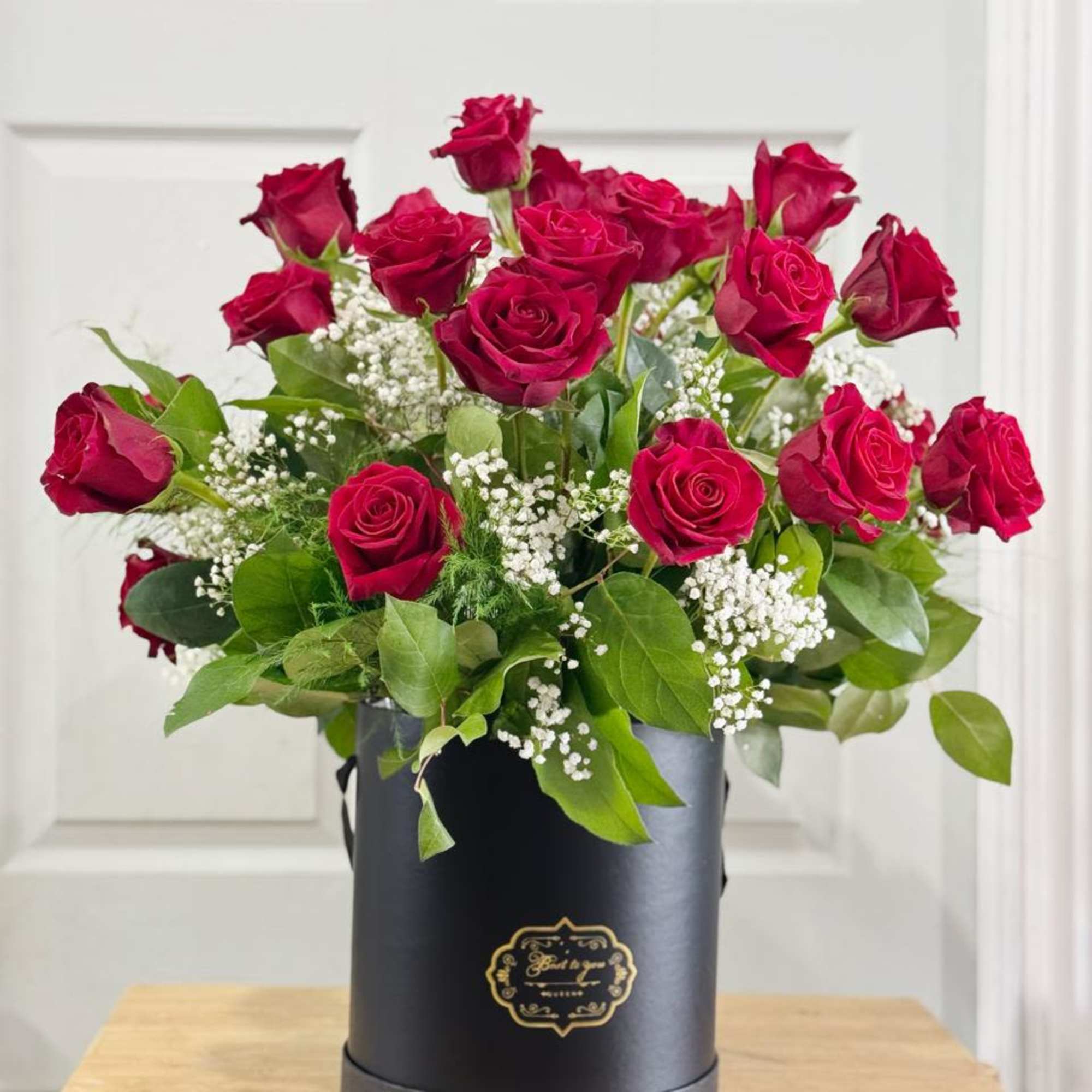 Red roses arranged in a black hat box with baby's breath