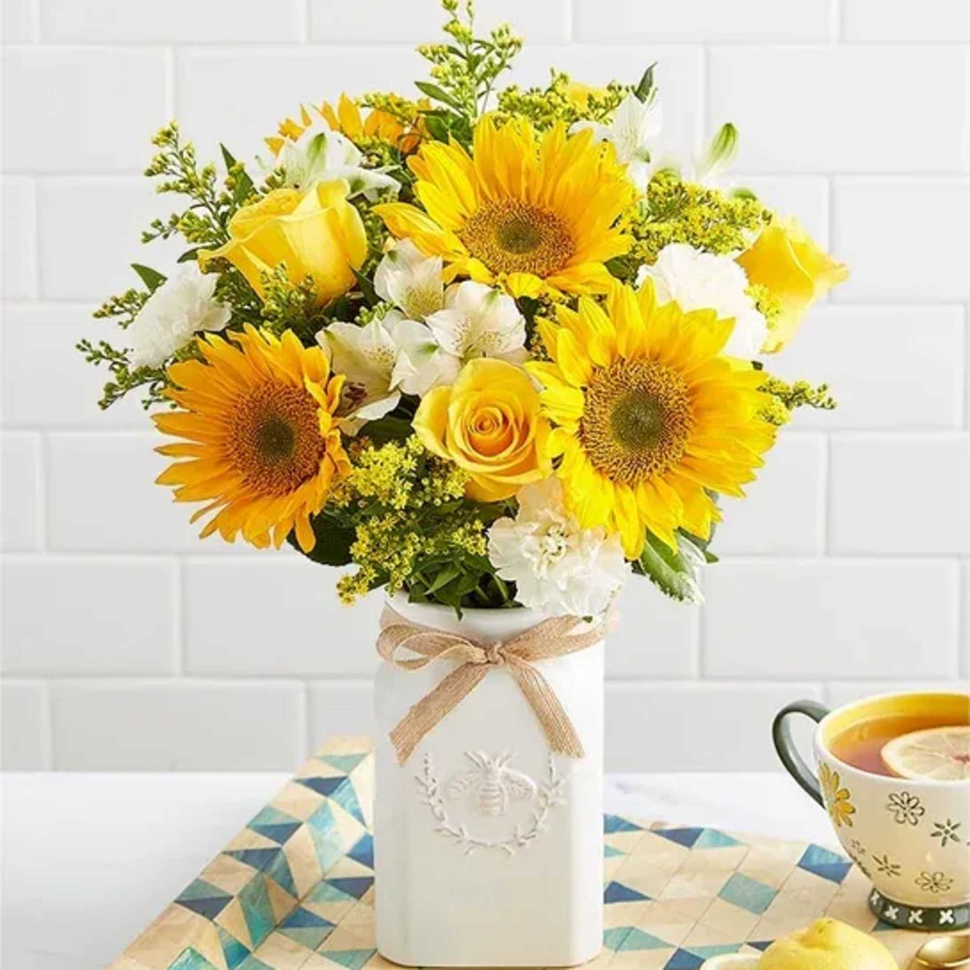 Yellow sunflowers and roses in a white vase with a ribbon