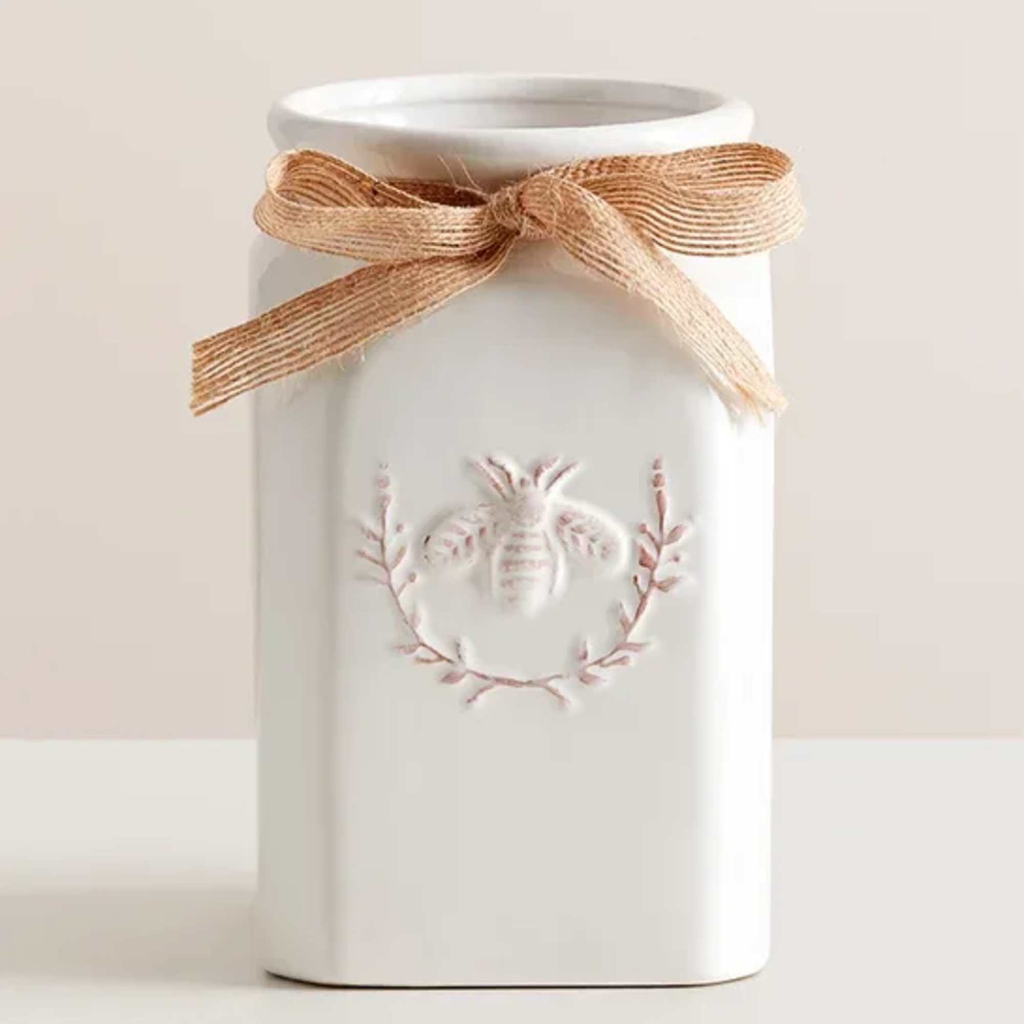 White ceramic jar with a tan ribbon bow and bee motif