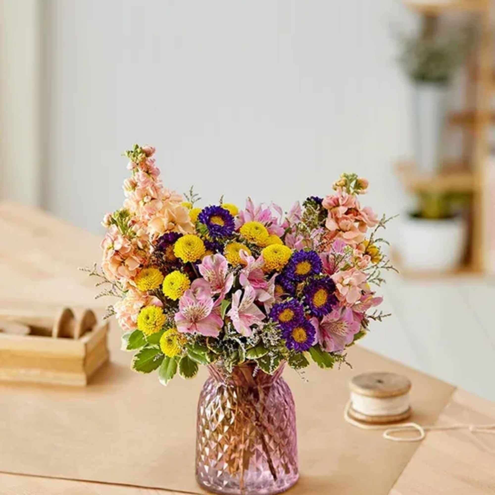 Mixed bouquet of pink, yellow, and purple flowers in a pink glass vase