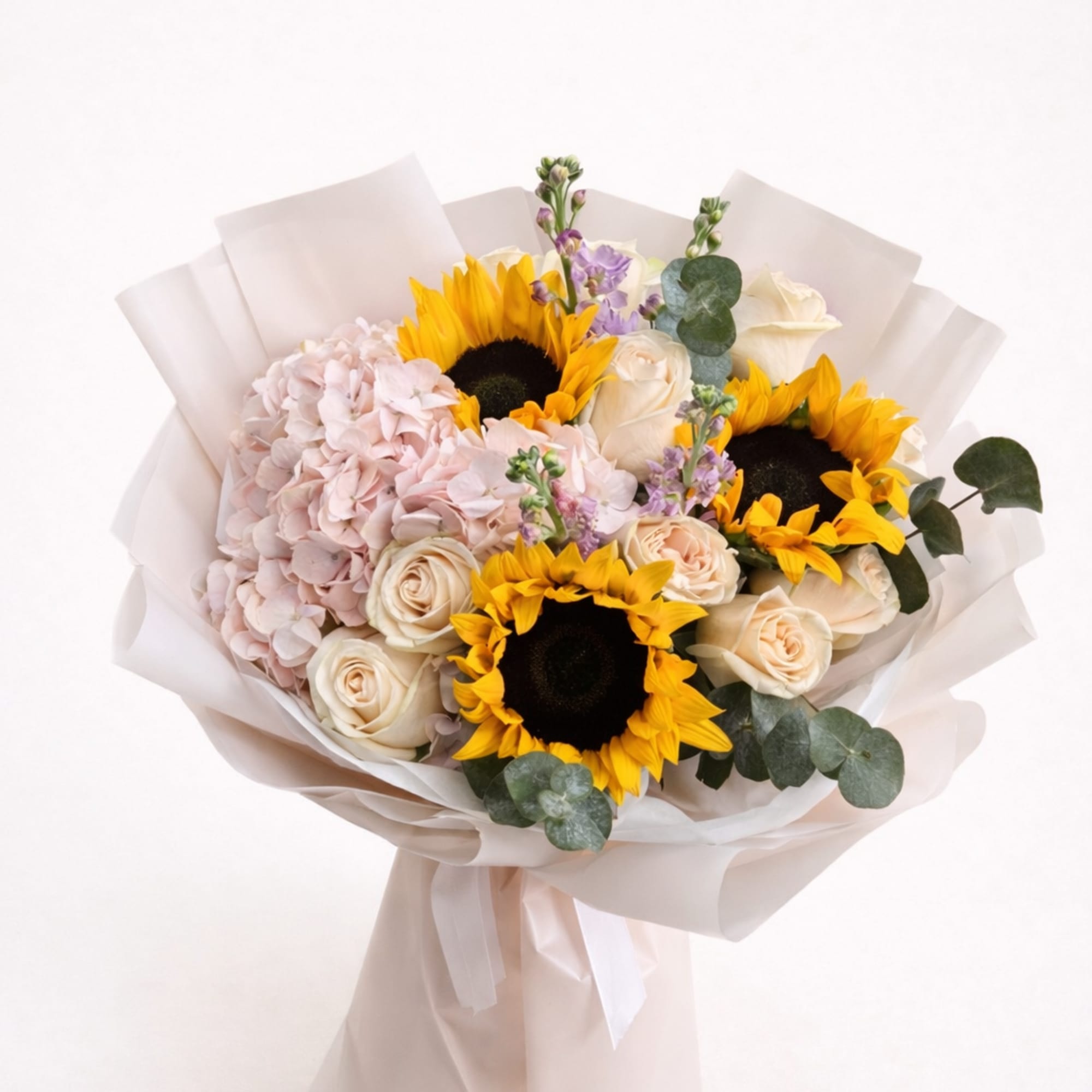 Bouquet of sunflowers, pale roses, and pink hydrangea wrapped in white paper