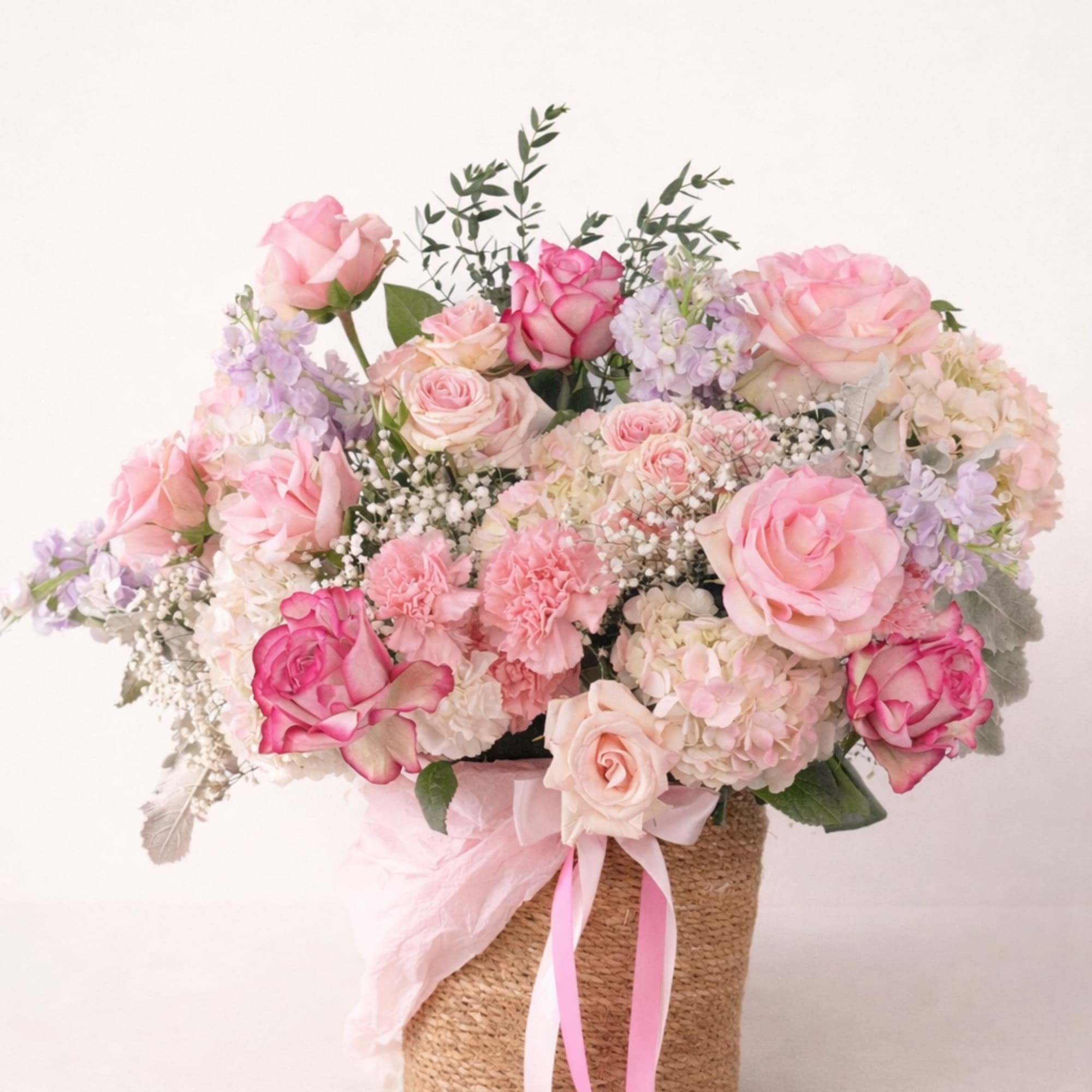 Pink and cream rose bouquet in a woven basket with ribbon