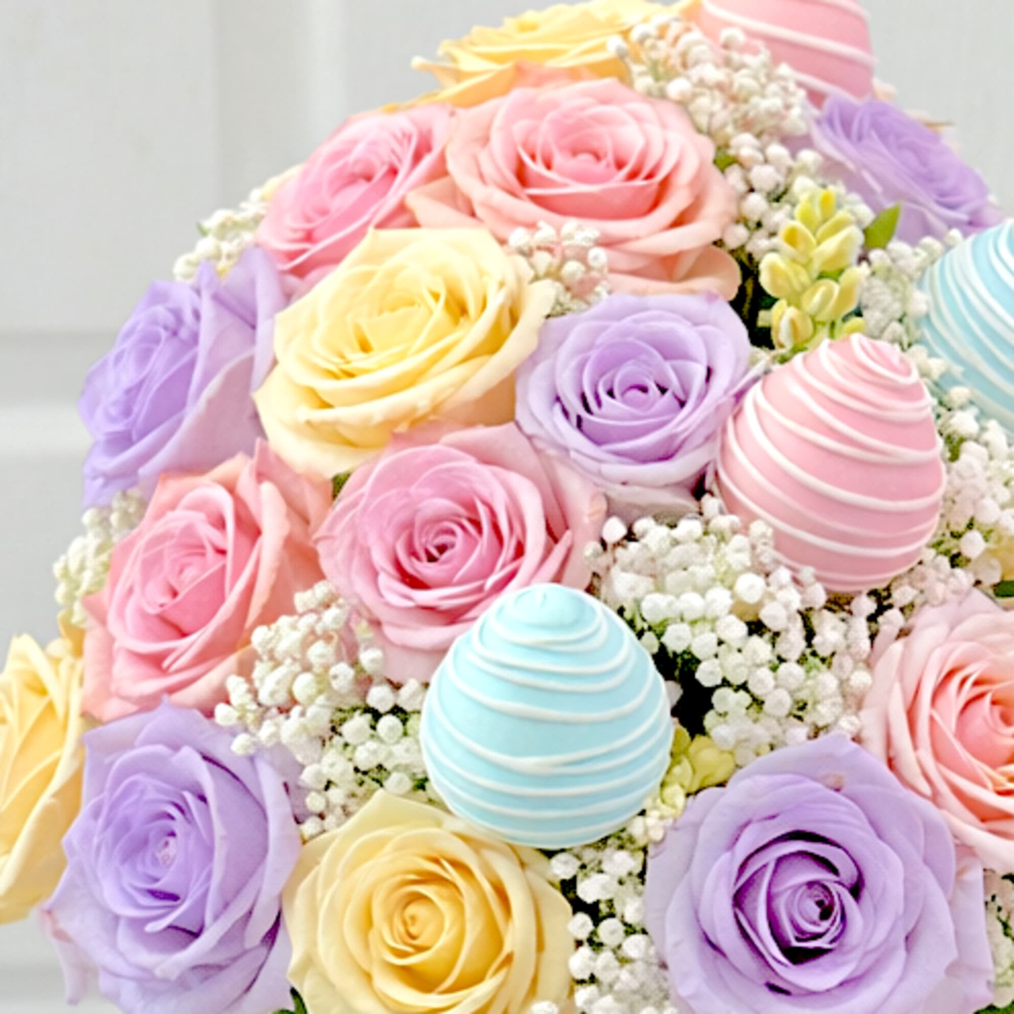 Pastel pink, yellow, and lavender roses with baby's breath and egg-shaped decorations in a white container