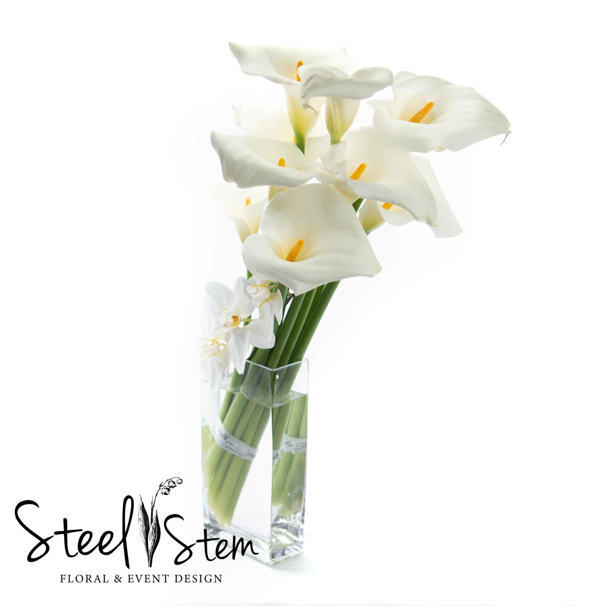 White love calla lilies burst out of a tall rectangular glass vase, photo 2 of 2
