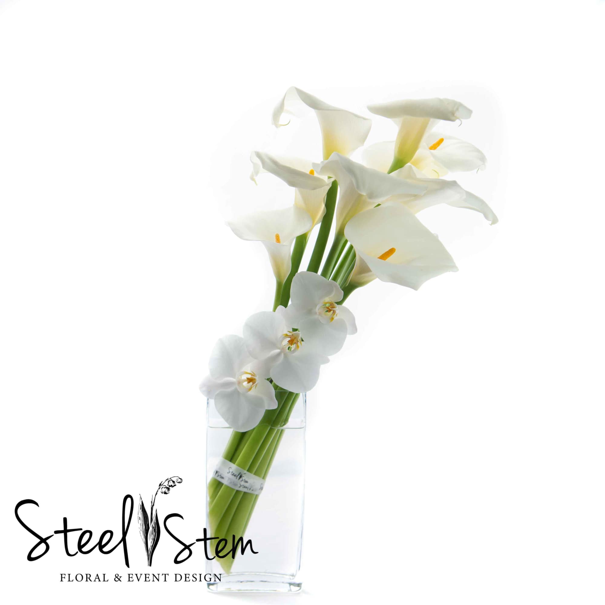 White love calla lilies burst out of a tall rectangular glass vase