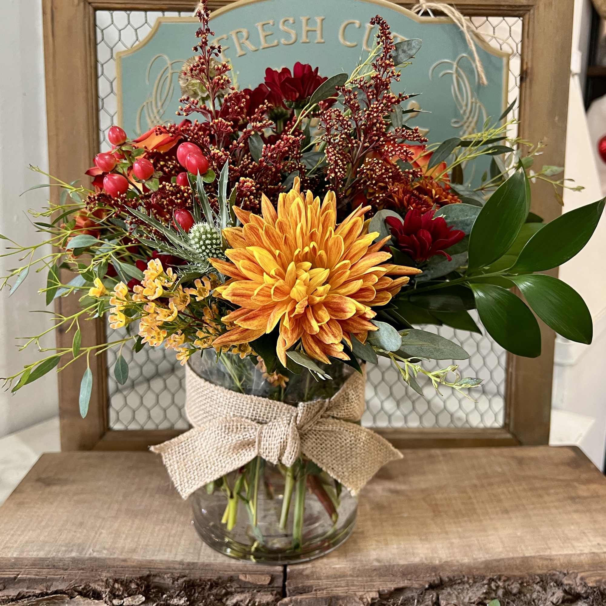 Mixed bouquet of orange, red, and yellow flowers in a glass vase with a burlap bow