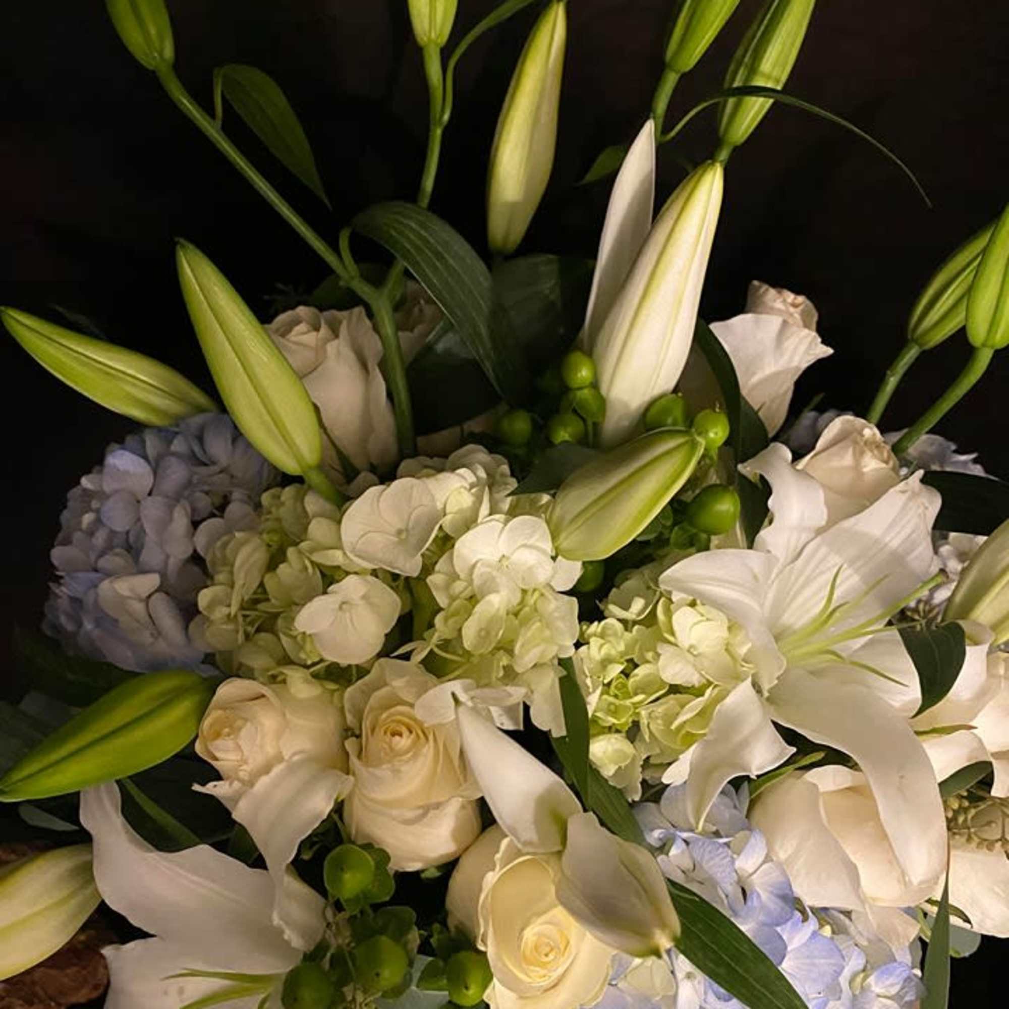 White lilies and roses with pale blue hydrangeas in a bouquet