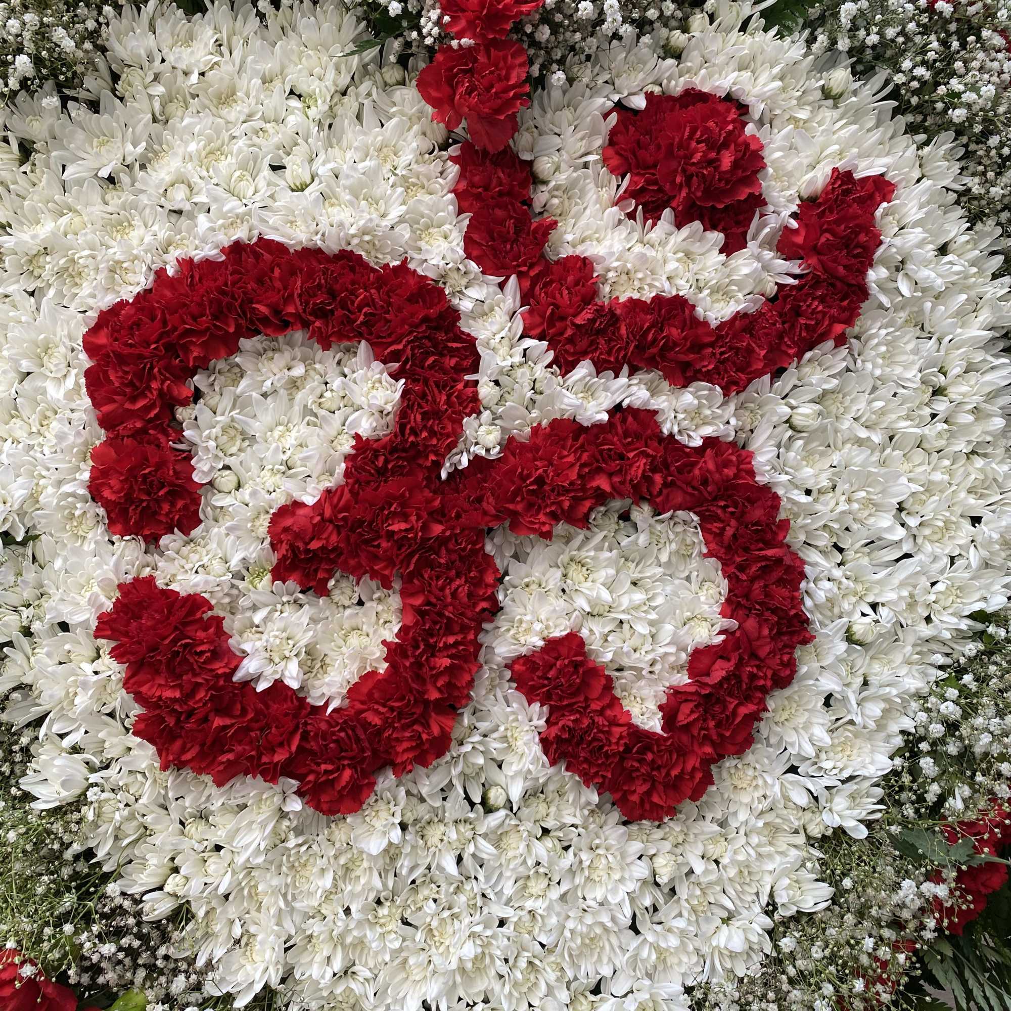 Large floral tribute with red lettering on a white chrysanthemum background
