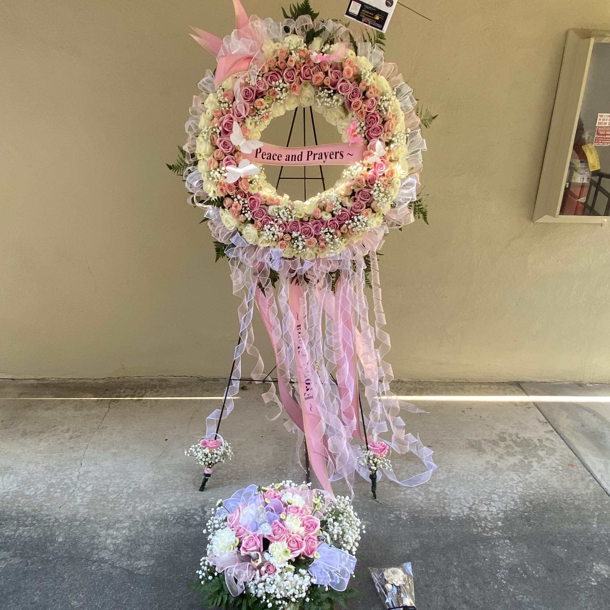 Pink and white floral standing wreath with ribbons and a "Peace and Prayers" sign