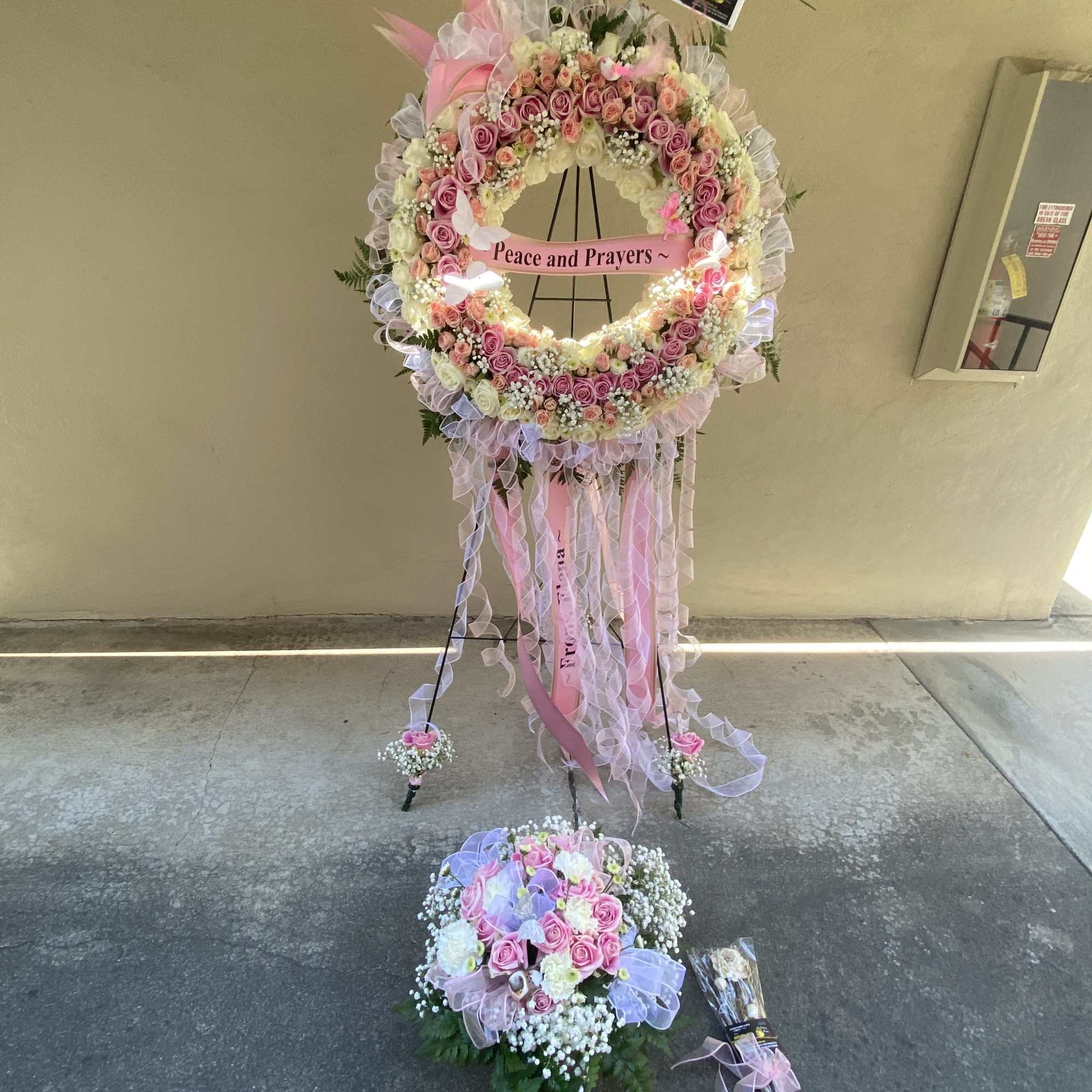 Large pink and white floral standing wreath with ribbons and a matching bouquet below