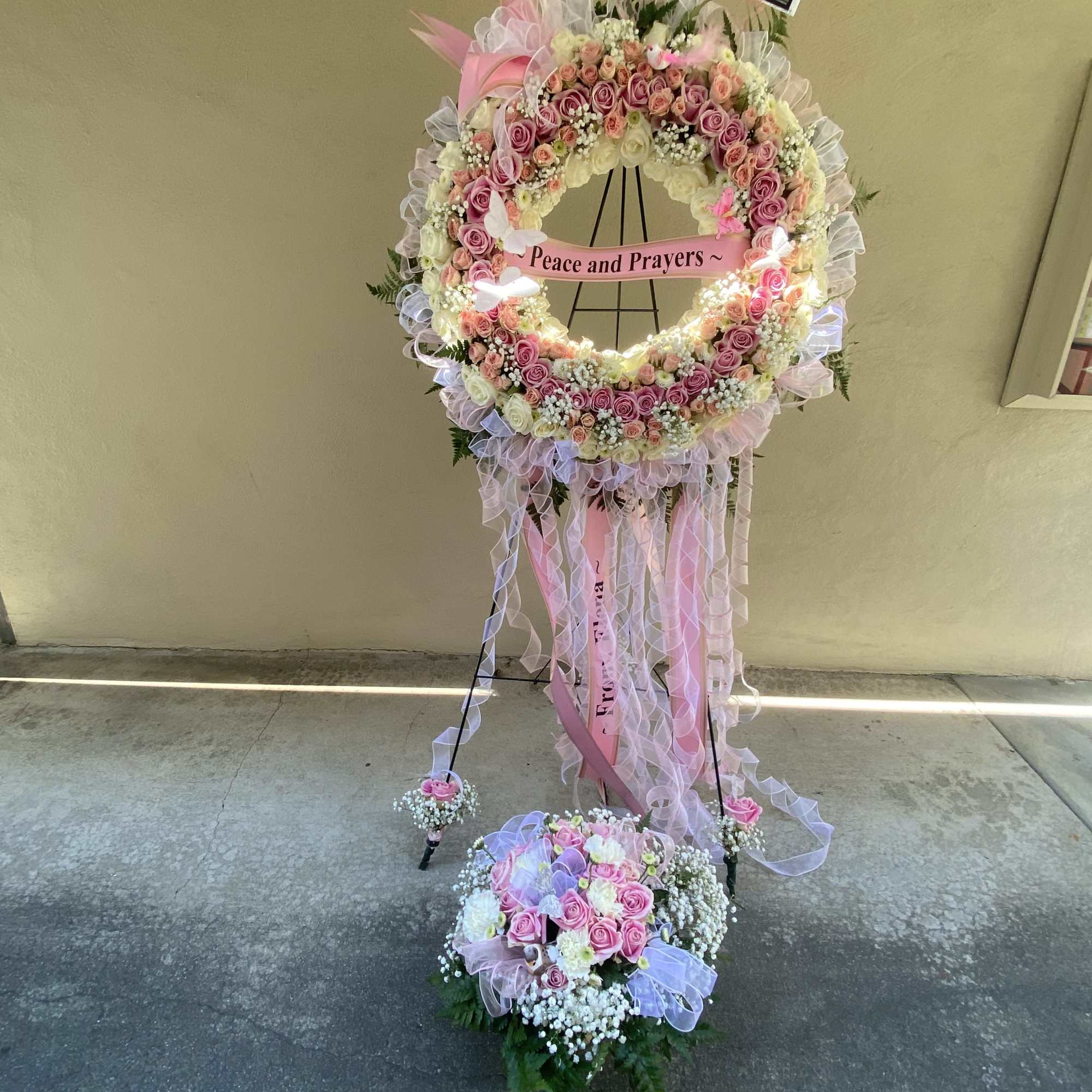 Pink and white floral standing wreath with ribbon and a "Peace and Prayers" sign